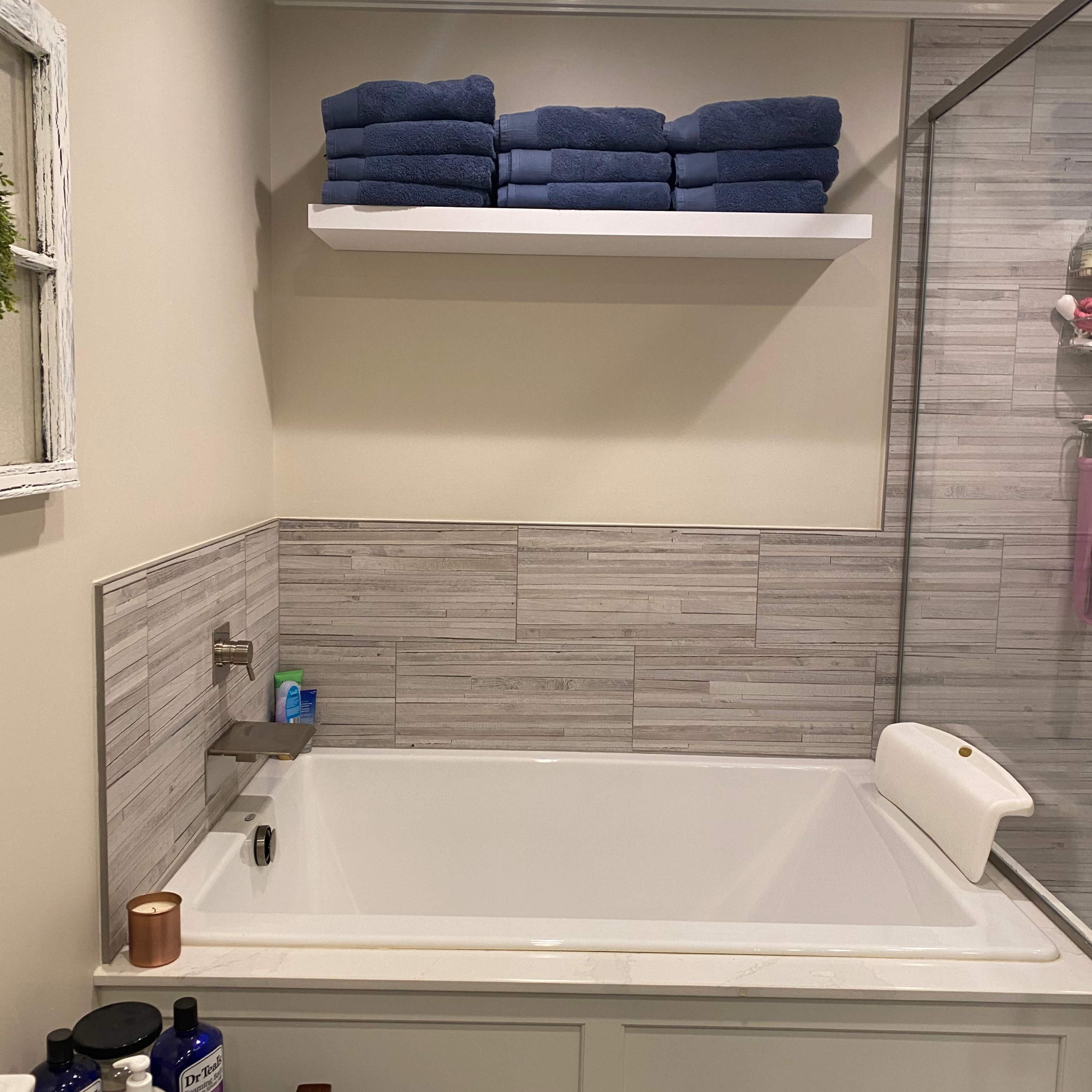 A clean bathroom with a white bathtub, a shelf stacked with blue towels, and a glass shower enclosure.