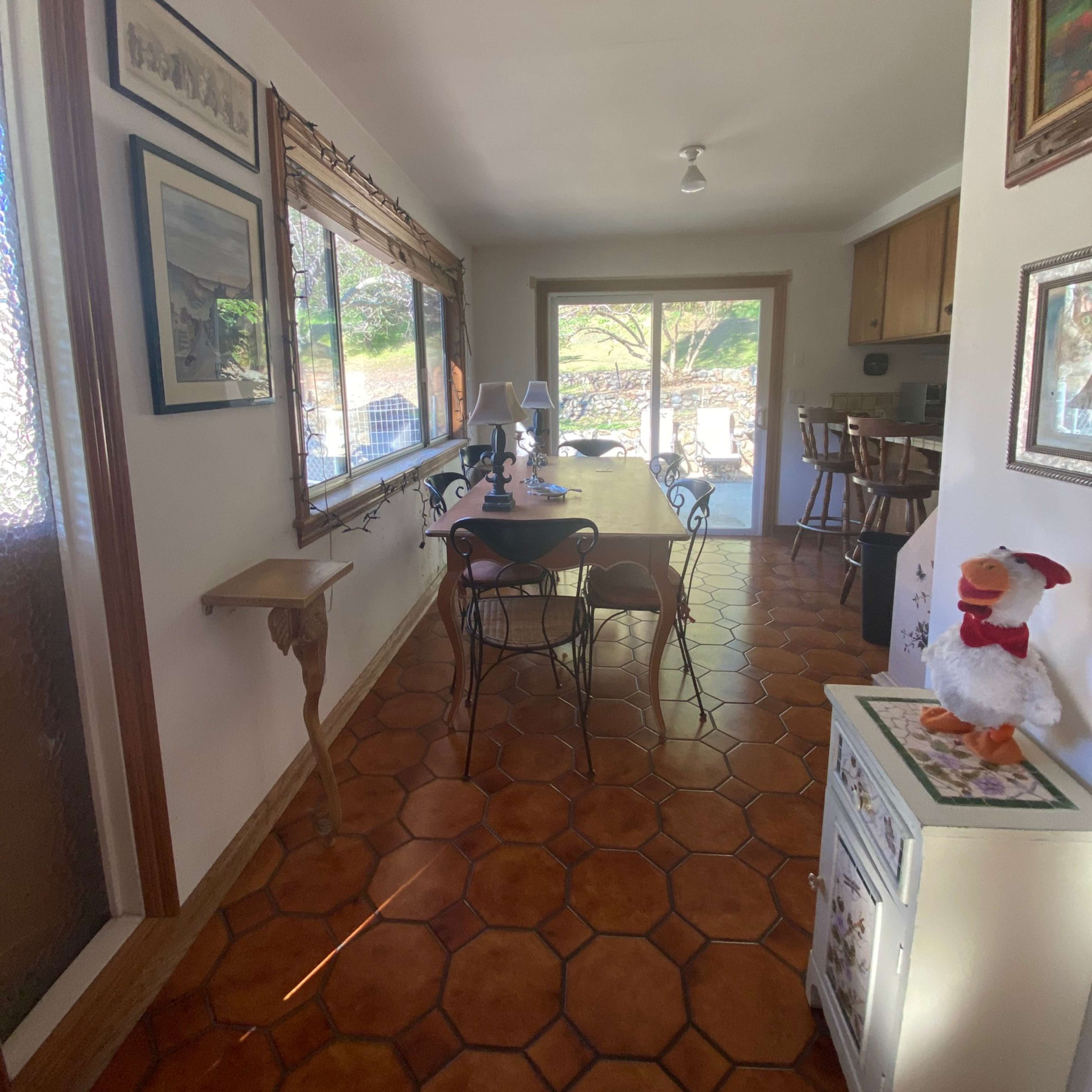 A dining area with a long table, surrounded by chairs, set in a room with tiled flooring and large windows that let in natural light.