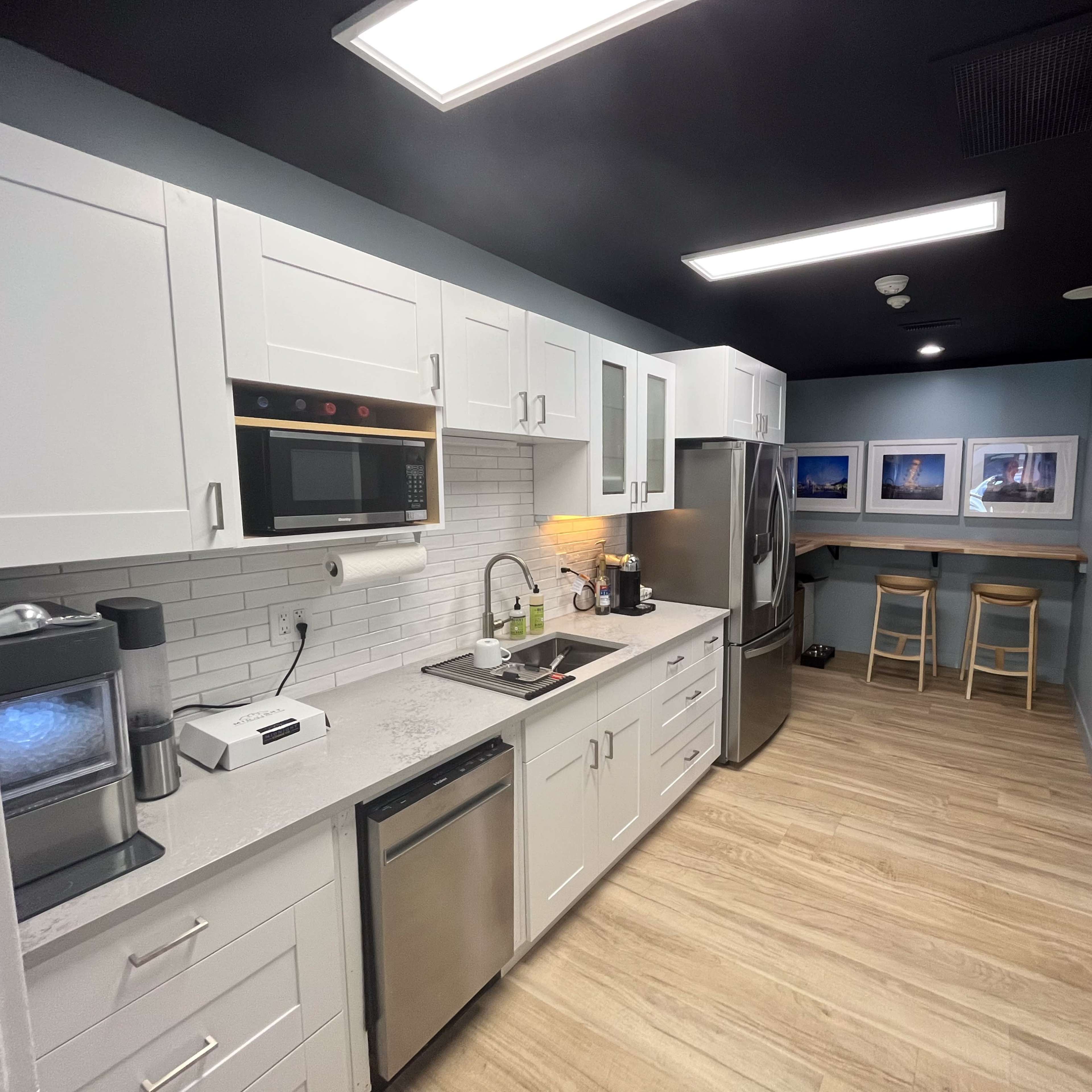 A modern kitchen featuring white cabinets, stainless steel appliances, and a bar with two stools in a well-lit space.