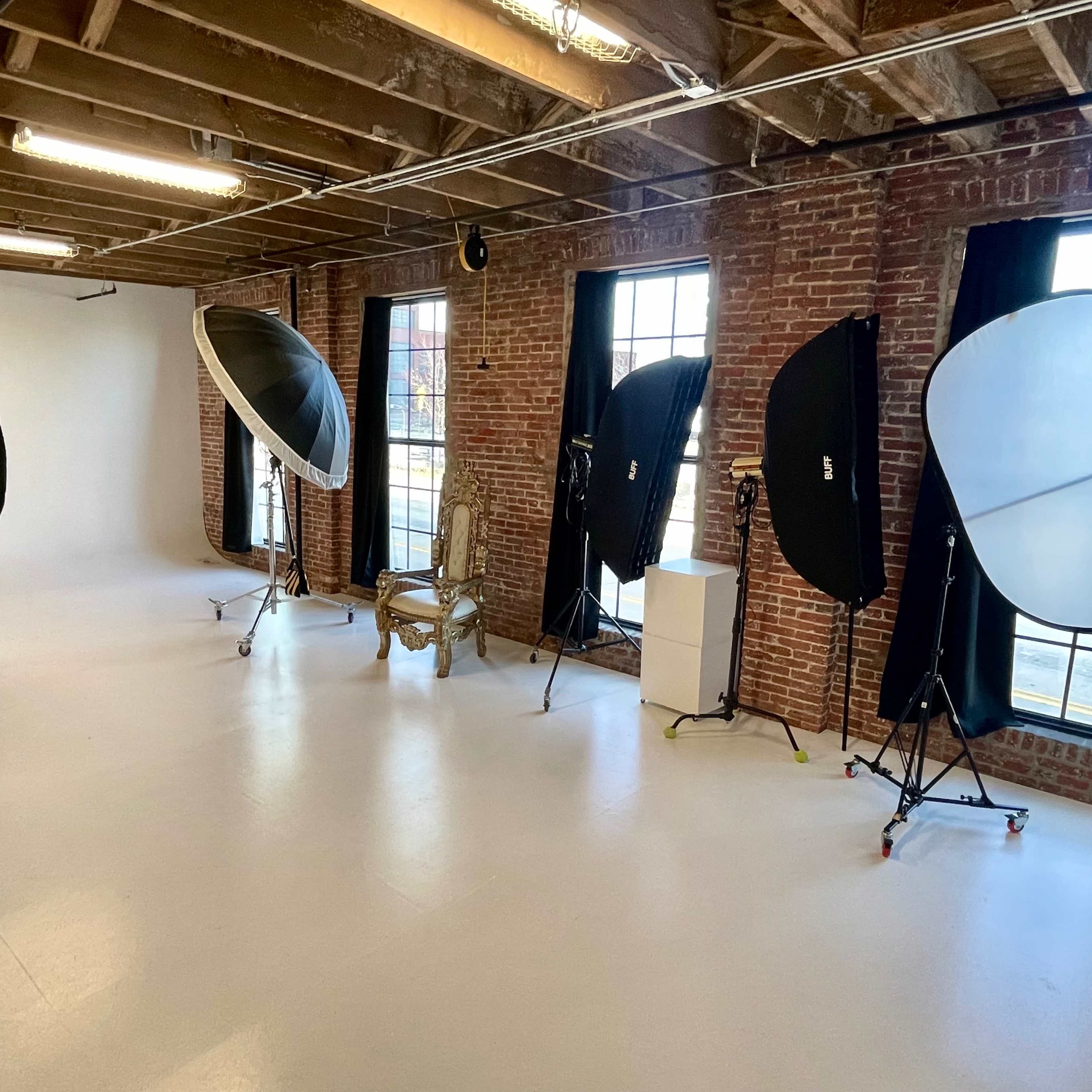 A photography studio with softboxes on stands, a vintage chair, and large windows allowing natural light.