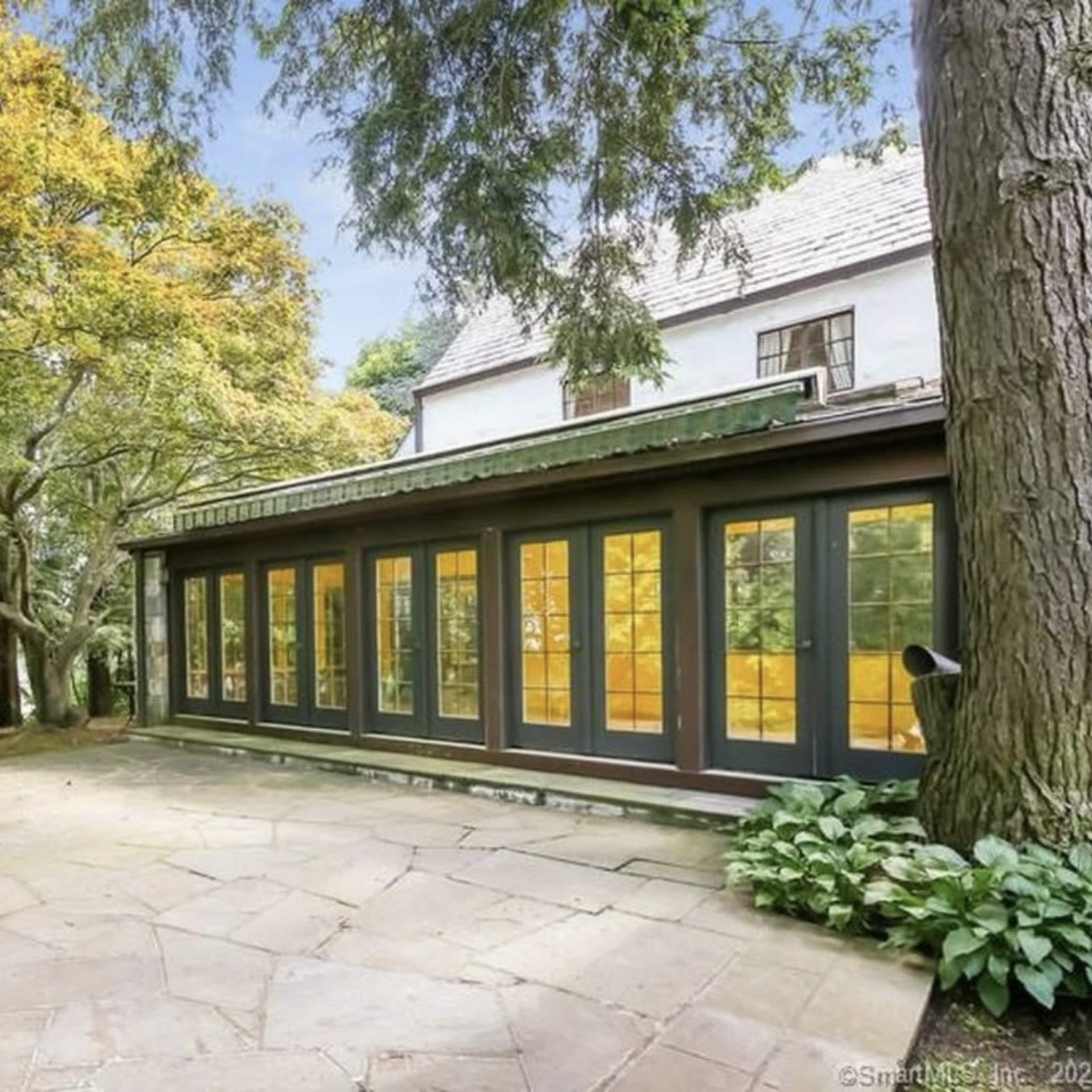 A stone patio area adjacent to a house, surrounded by trees and featuring large windows on one side.