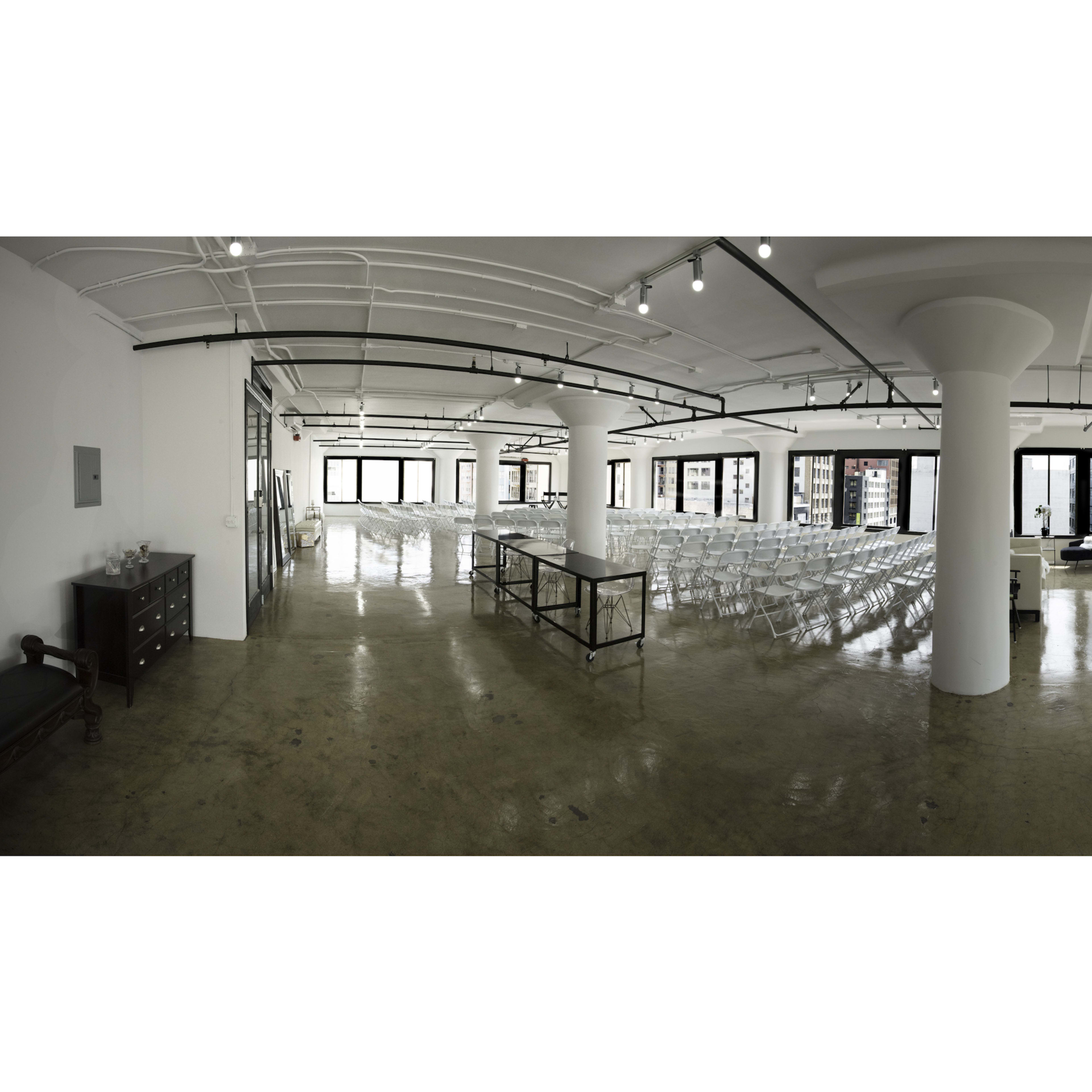 A spacious, empty event venue with rows of chairs set up, large windows, and a polished concrete floor.