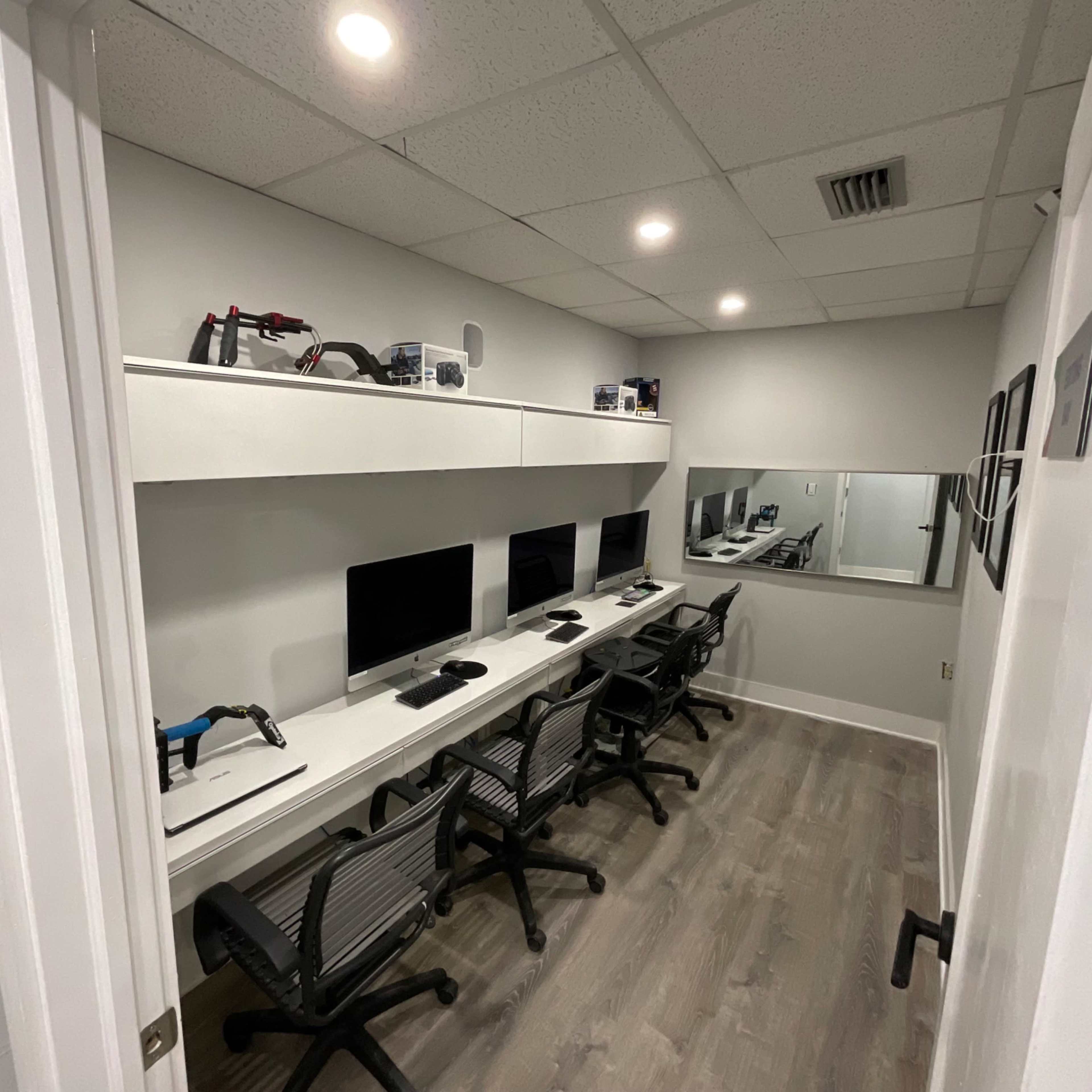 A minimalist office space with four computers arranged on a white desk, along with tools and a mirror on the wall.