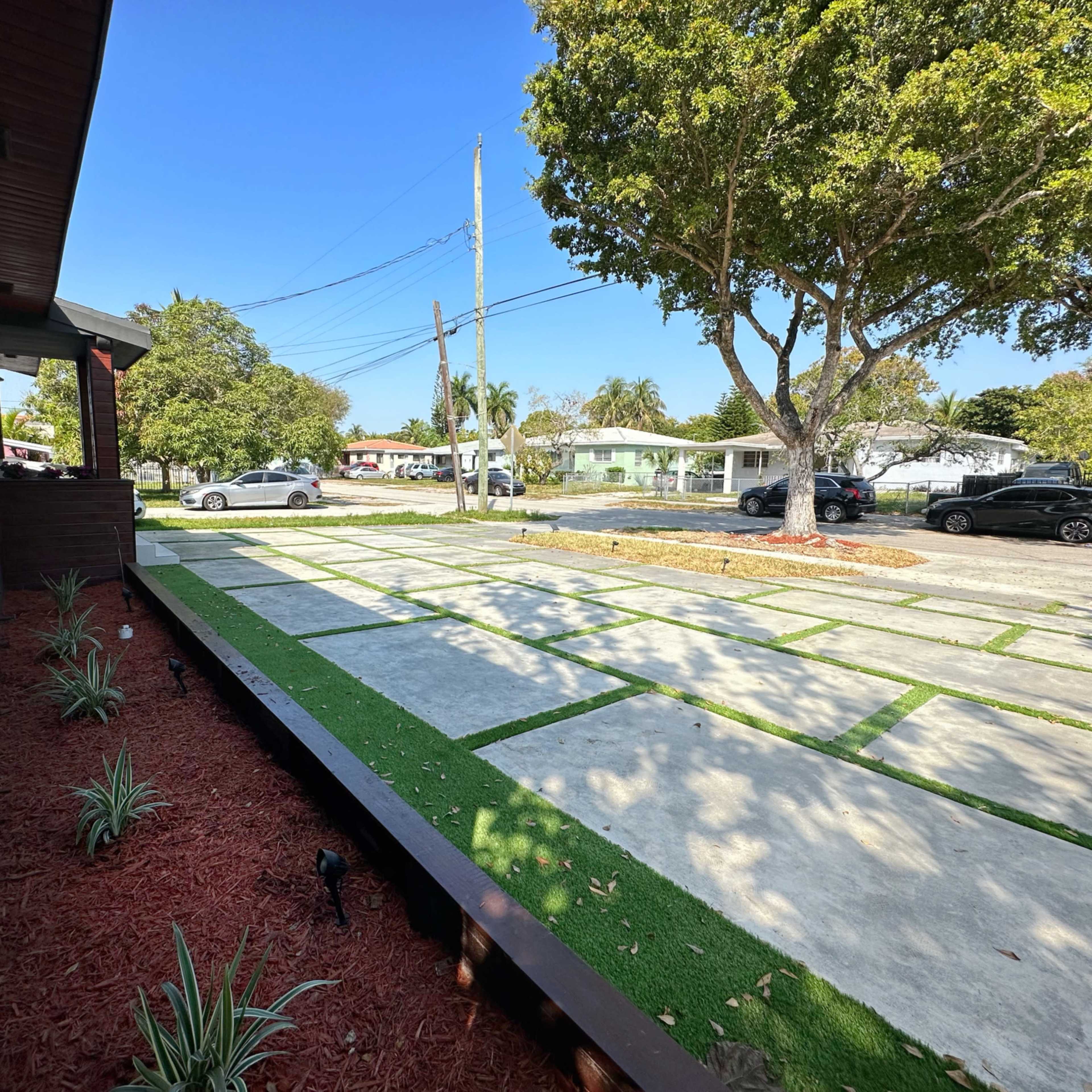 A rectangular concrete driveway bordered by grassy patches and surrounded by trees, with a clear view of a residential street.