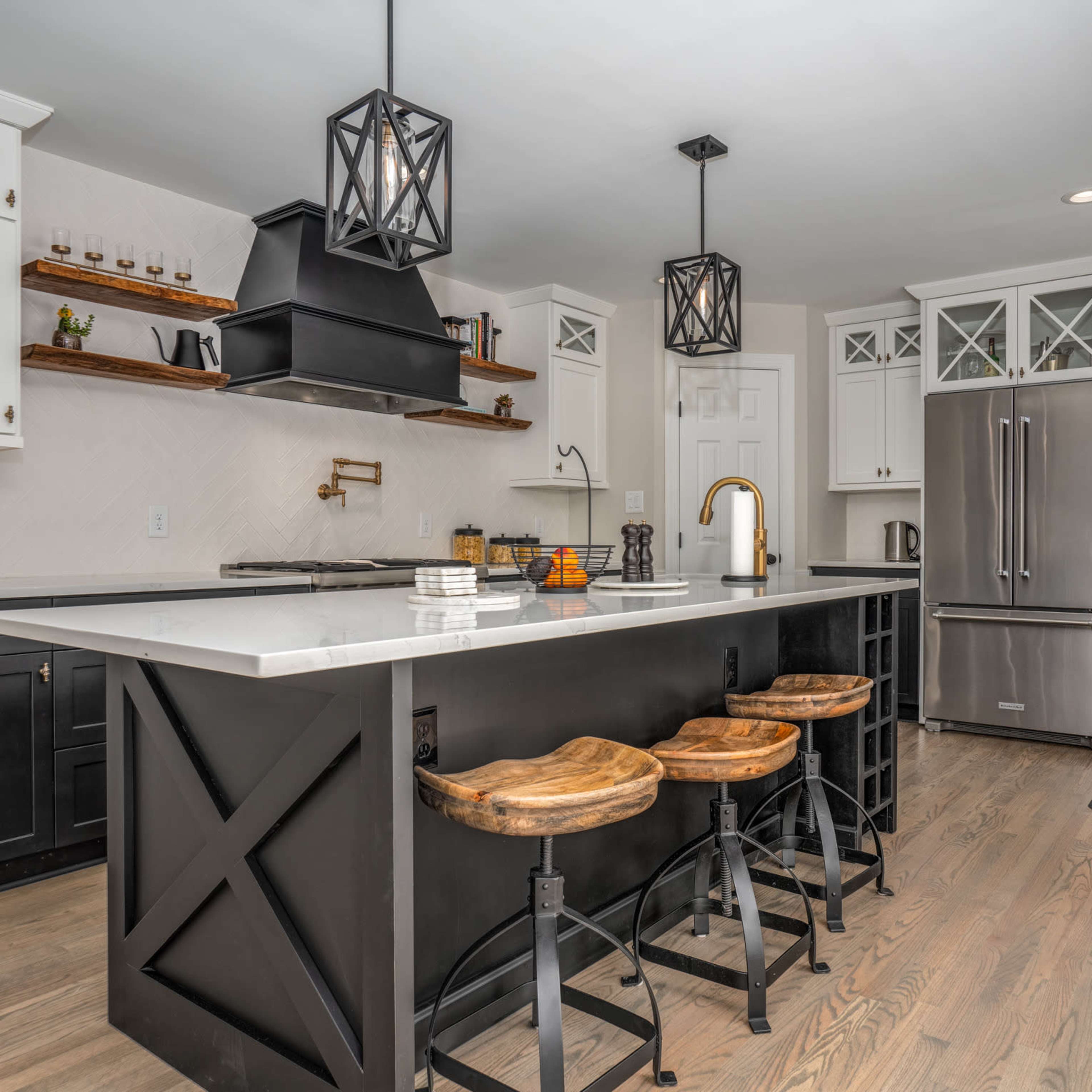 A modern kitchen with a central island, bar stools, pendant lights, and a mix of black and white cabinetry.