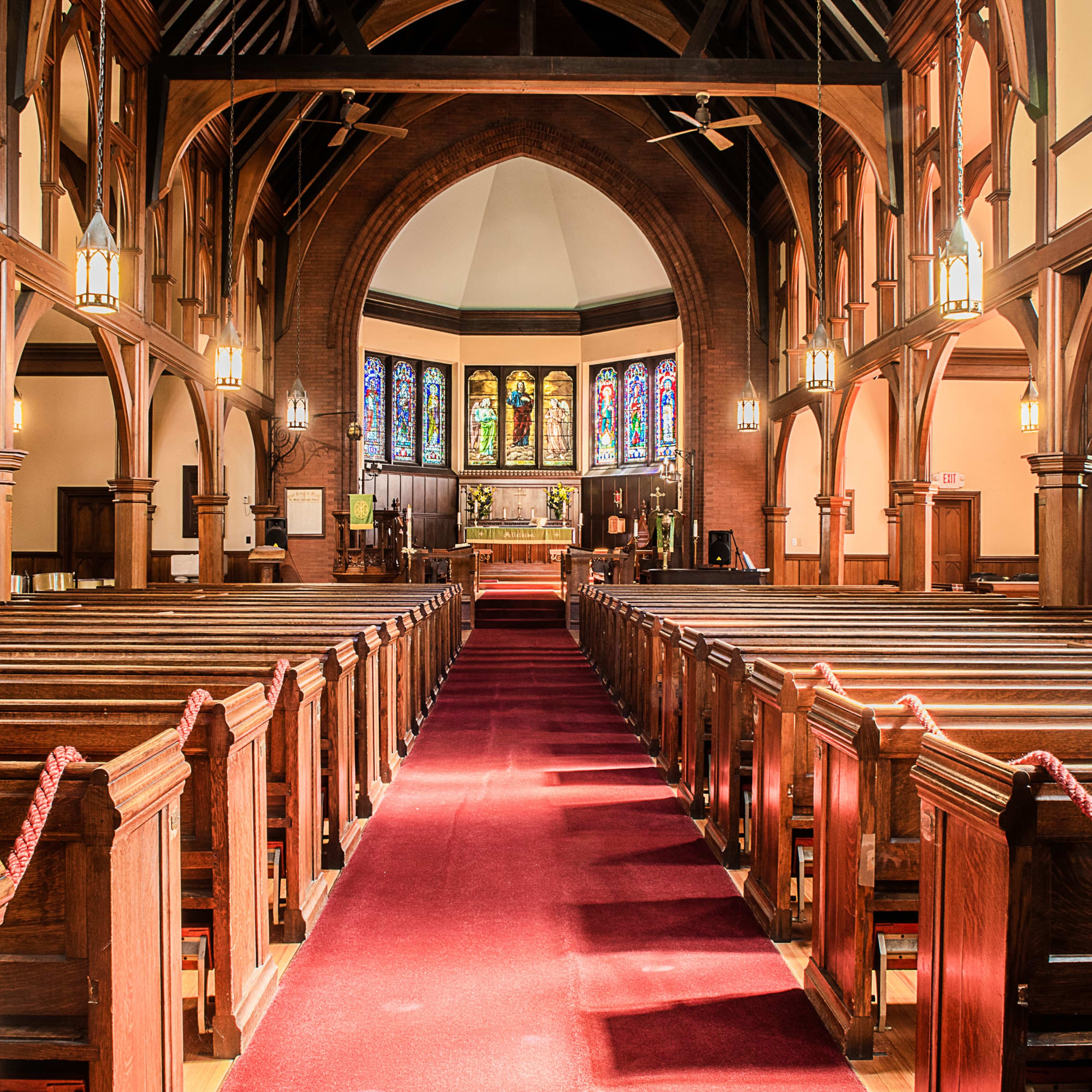 The interior of a church features wooden pews arranged along a central aisle leading to a raised altar beneath stained glass windows.