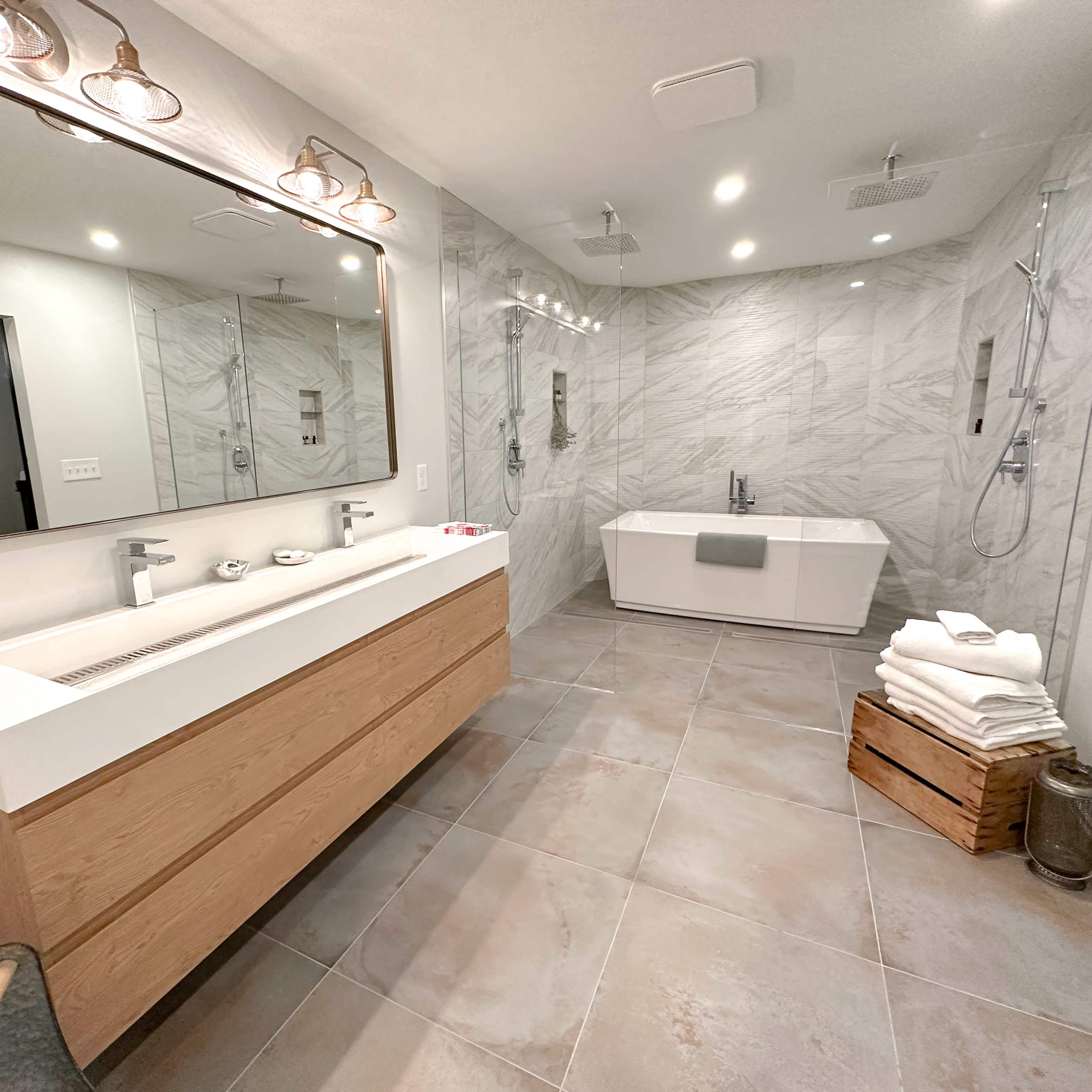 A modern bathroom featuring a freestanding tub, a double vanity with a large mirror, and gray marble walls.