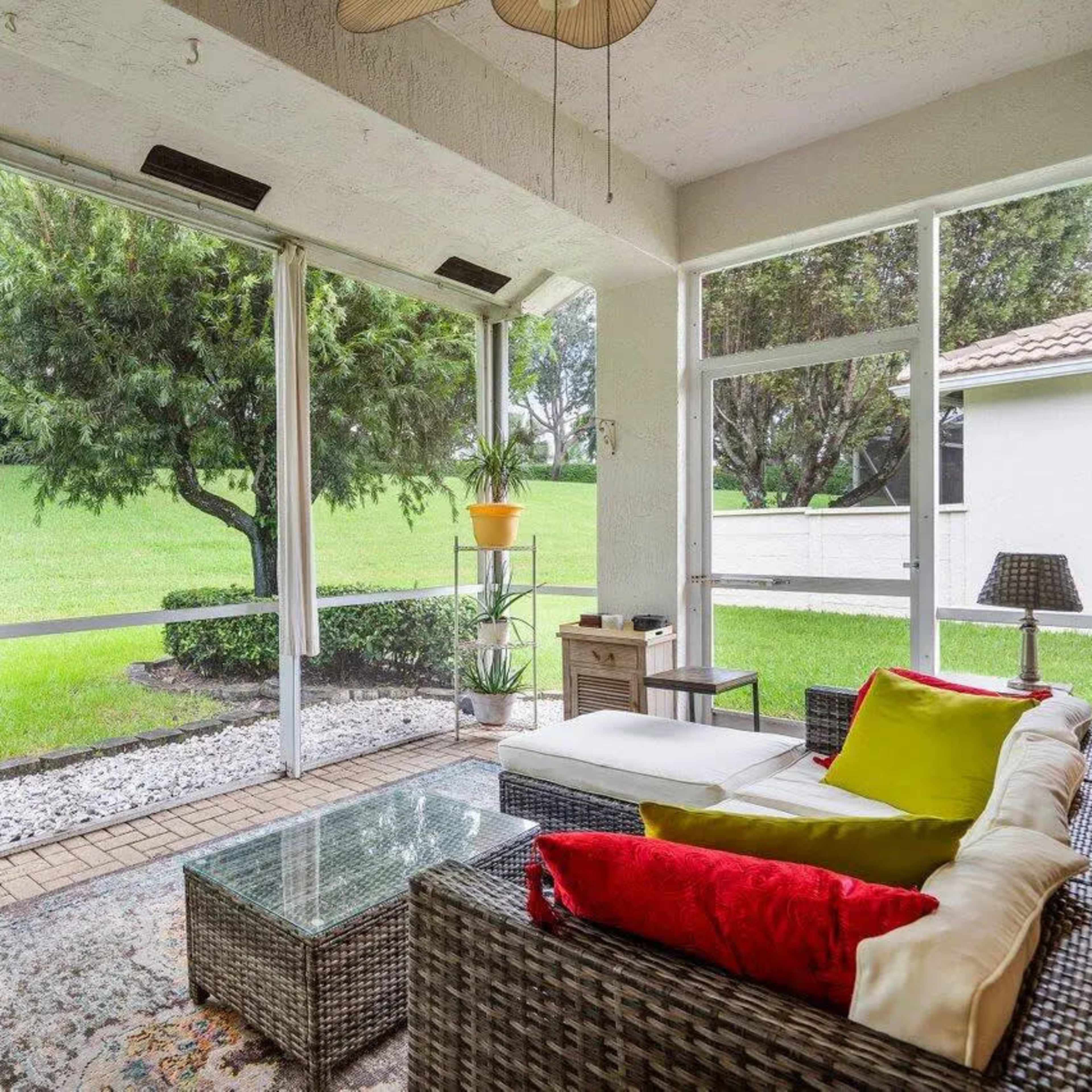 A screened-in porch with a wicker seating area, a glass coffee table, and greenery visible through the screens.