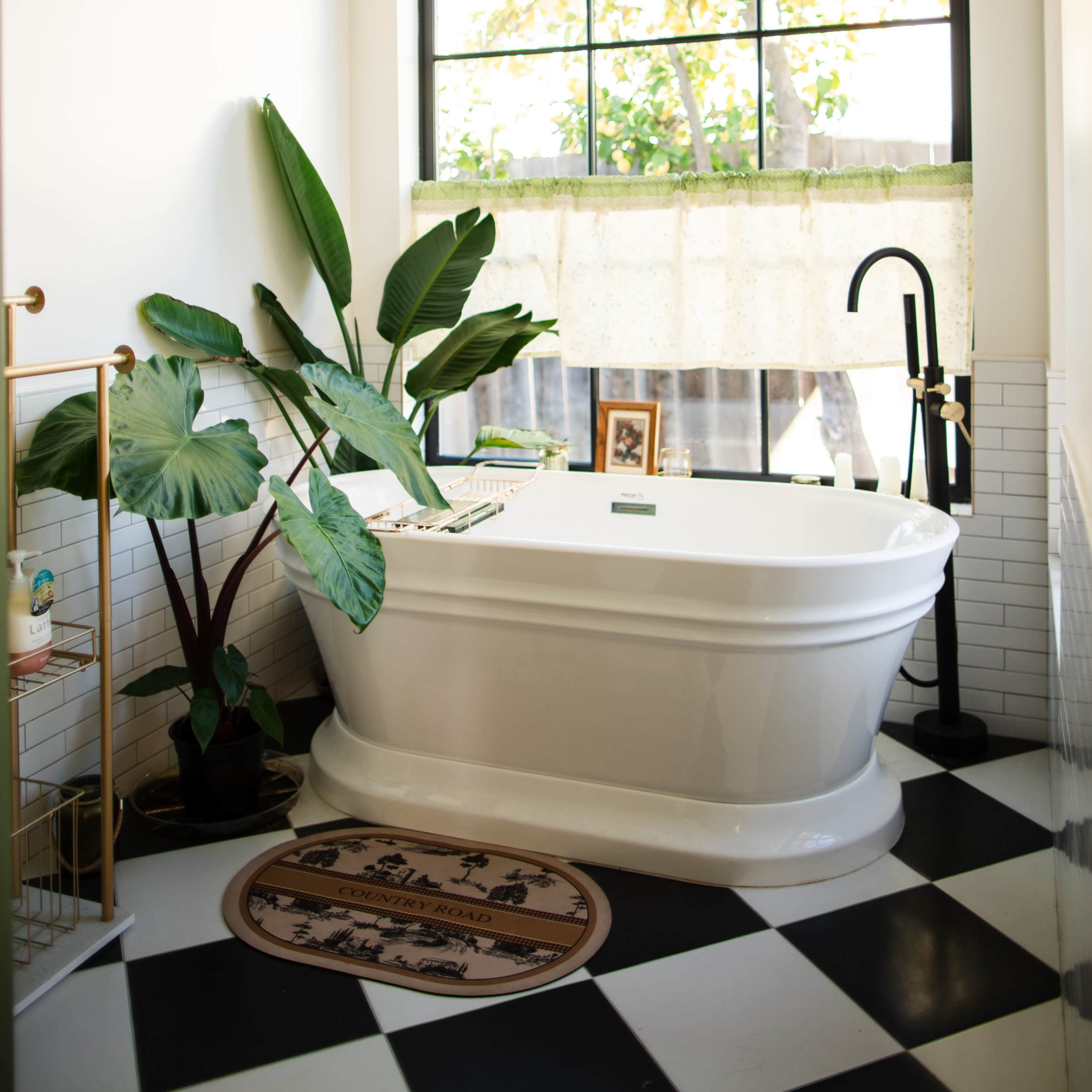 A modern bathroom featuring a freestanding bathtub, large window with greenery outside, and a black and white checkered floor.