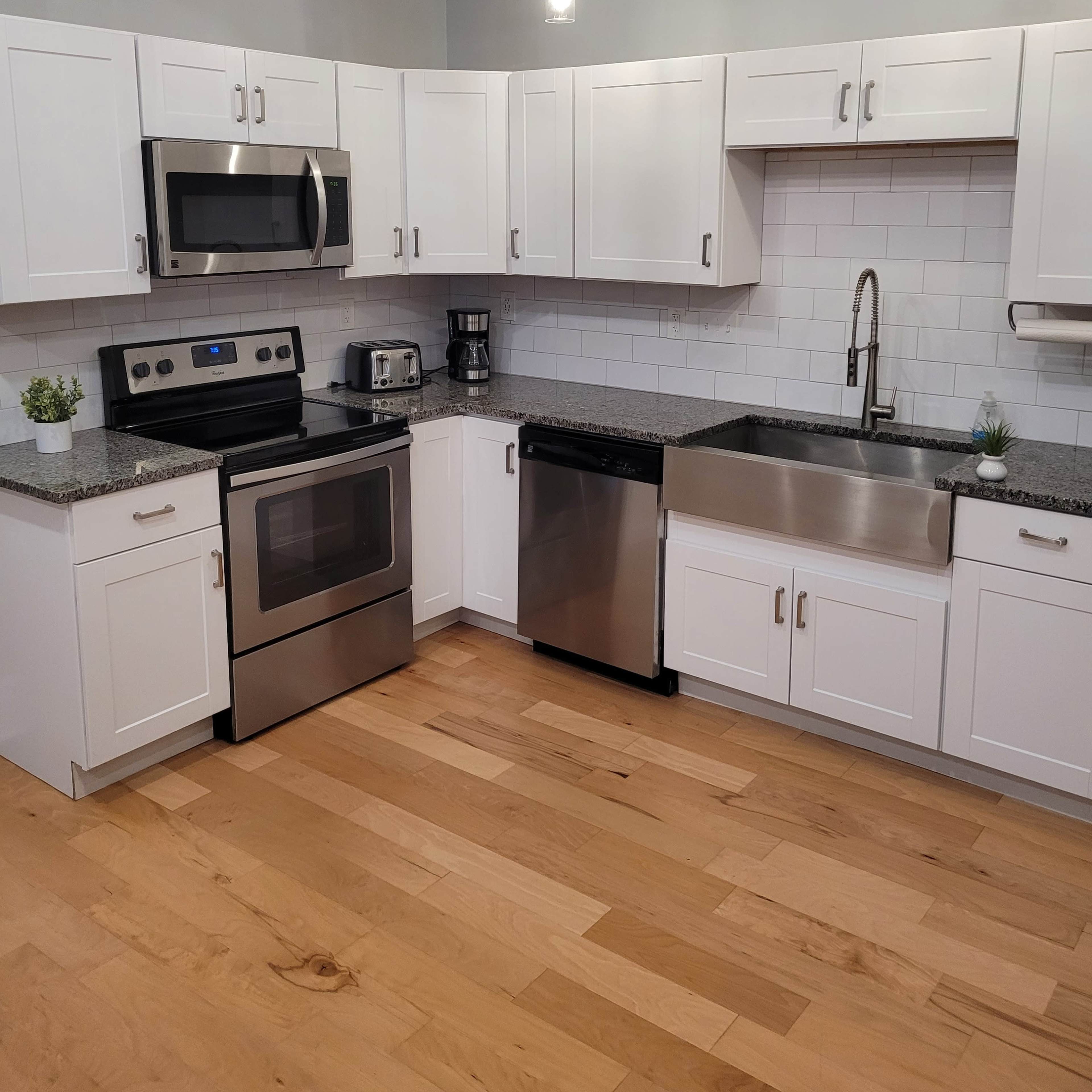 A modern kitchen with white cabinets, stainless steel appliances, and a large sink, featuring a light wood floor.