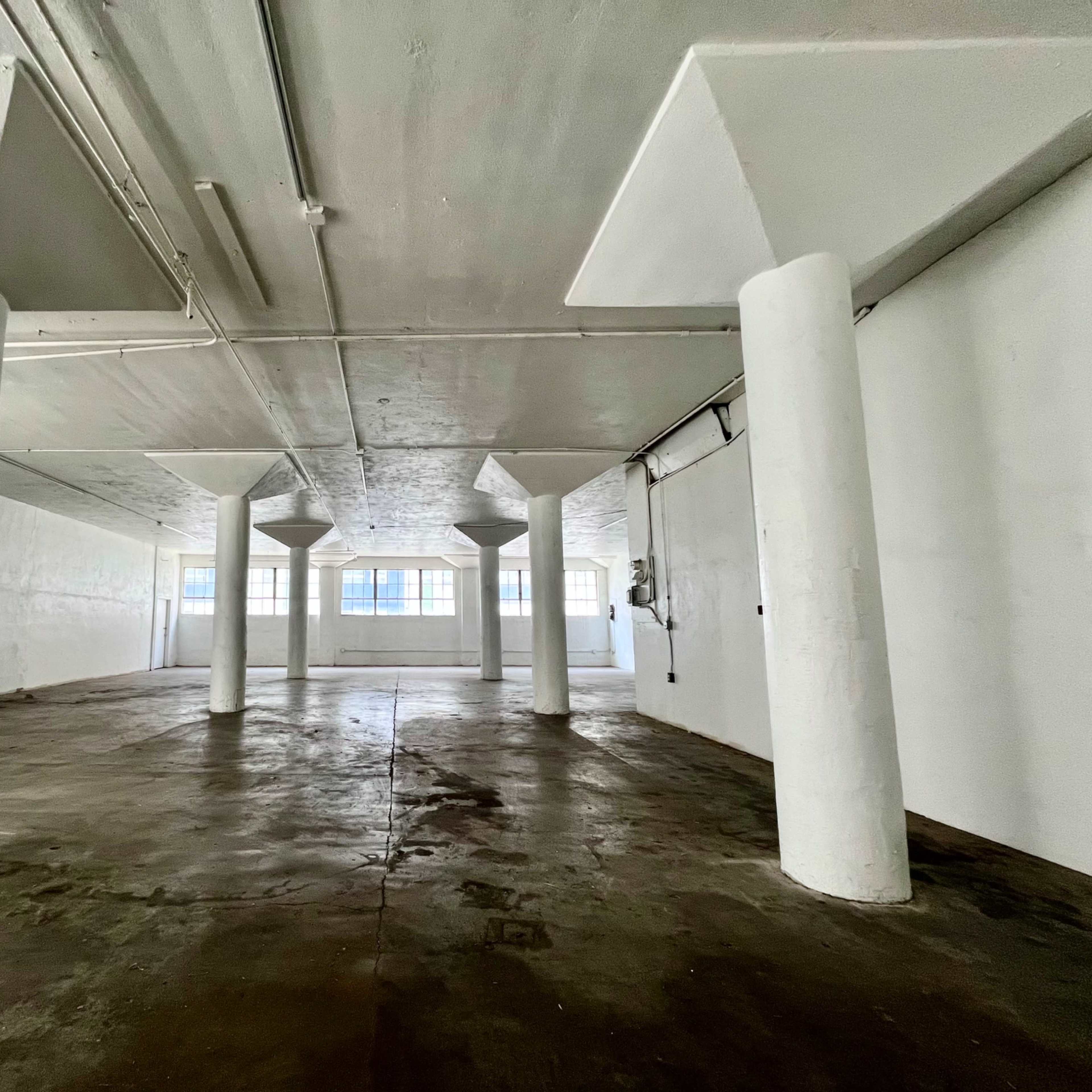 An empty, industrial-style room with concrete floors and several white support pillars.