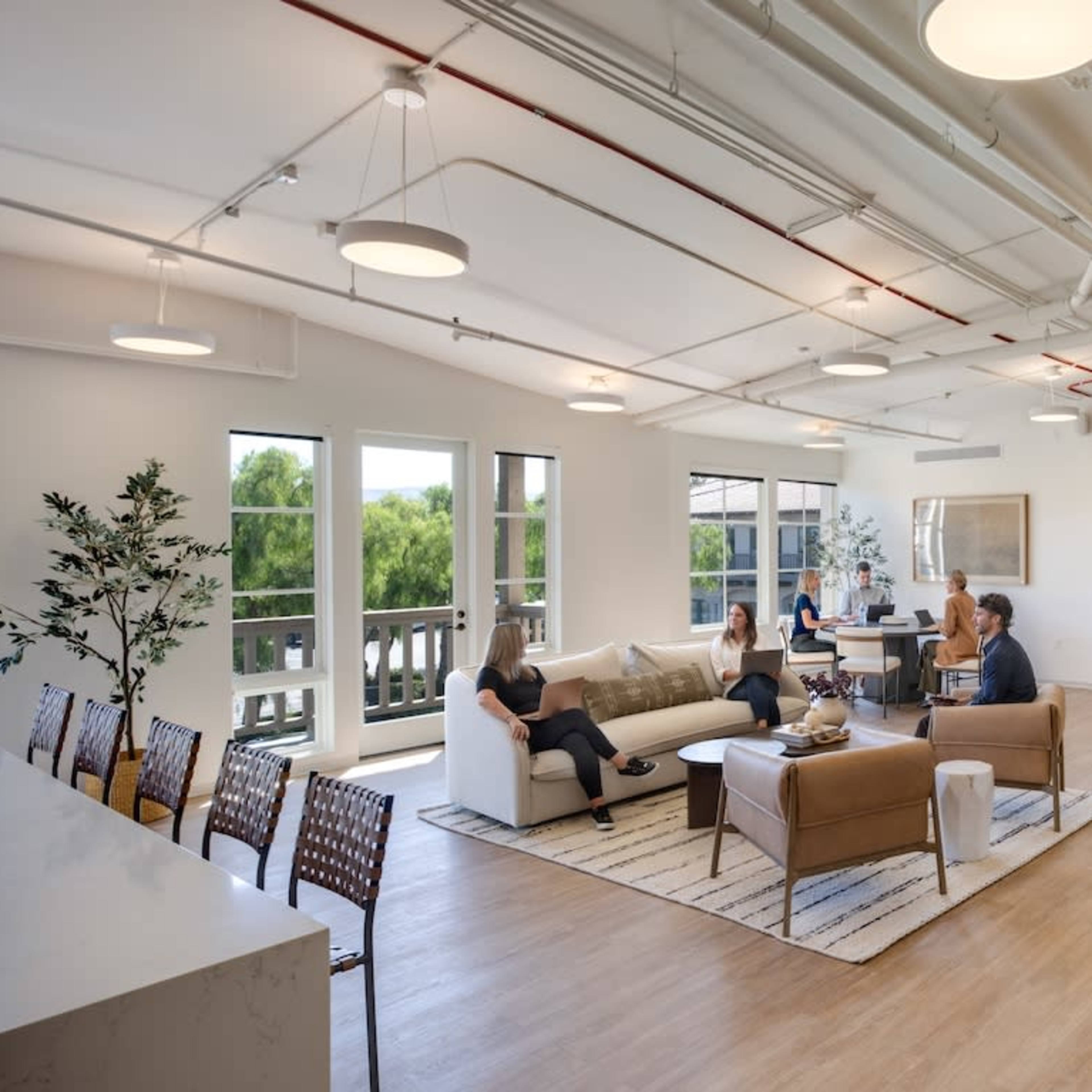 A modern office space with a reception area, seating arrangements, and several people engaged in various activities.