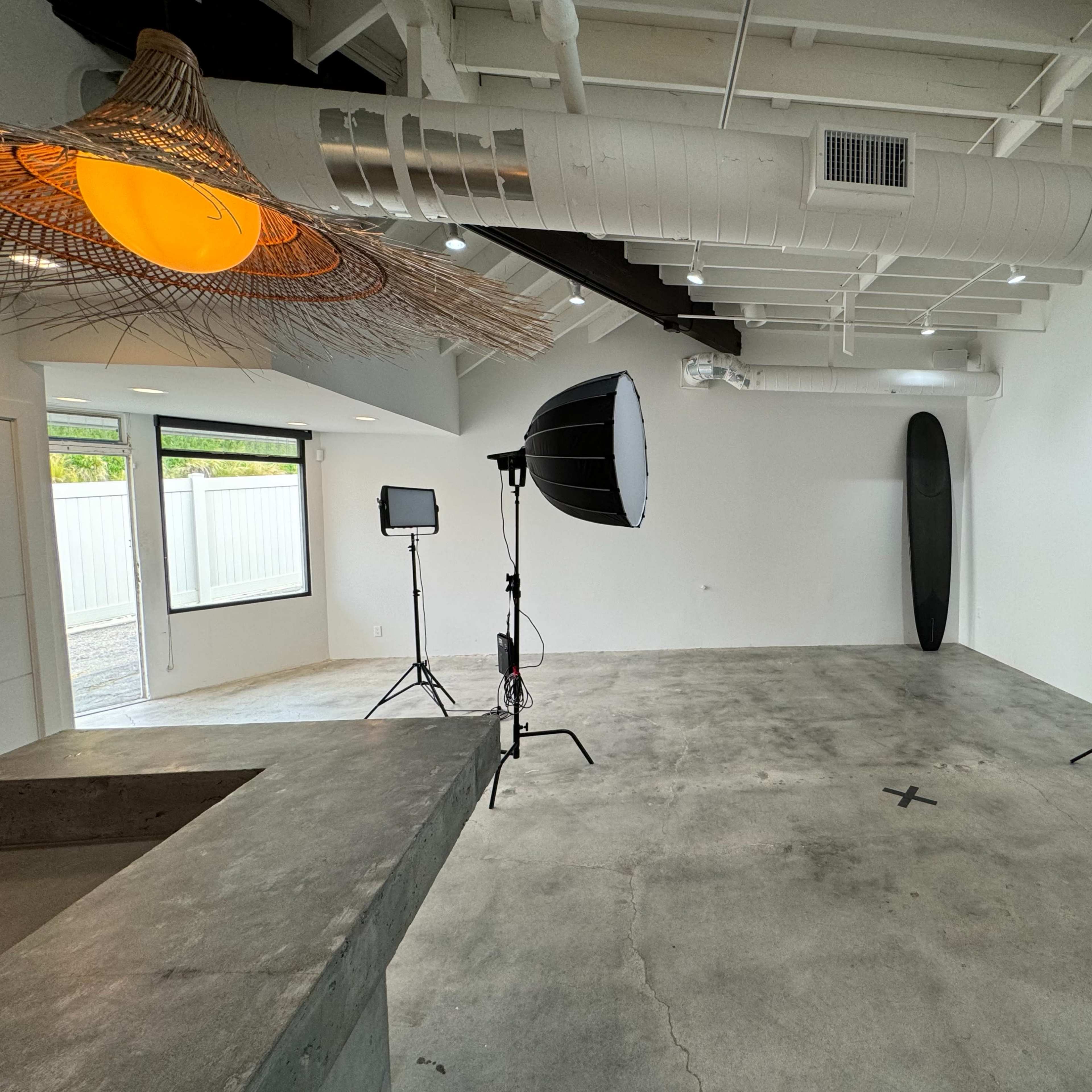 An empty studio space with two softbox lights and a surfboard leaning against the wall.