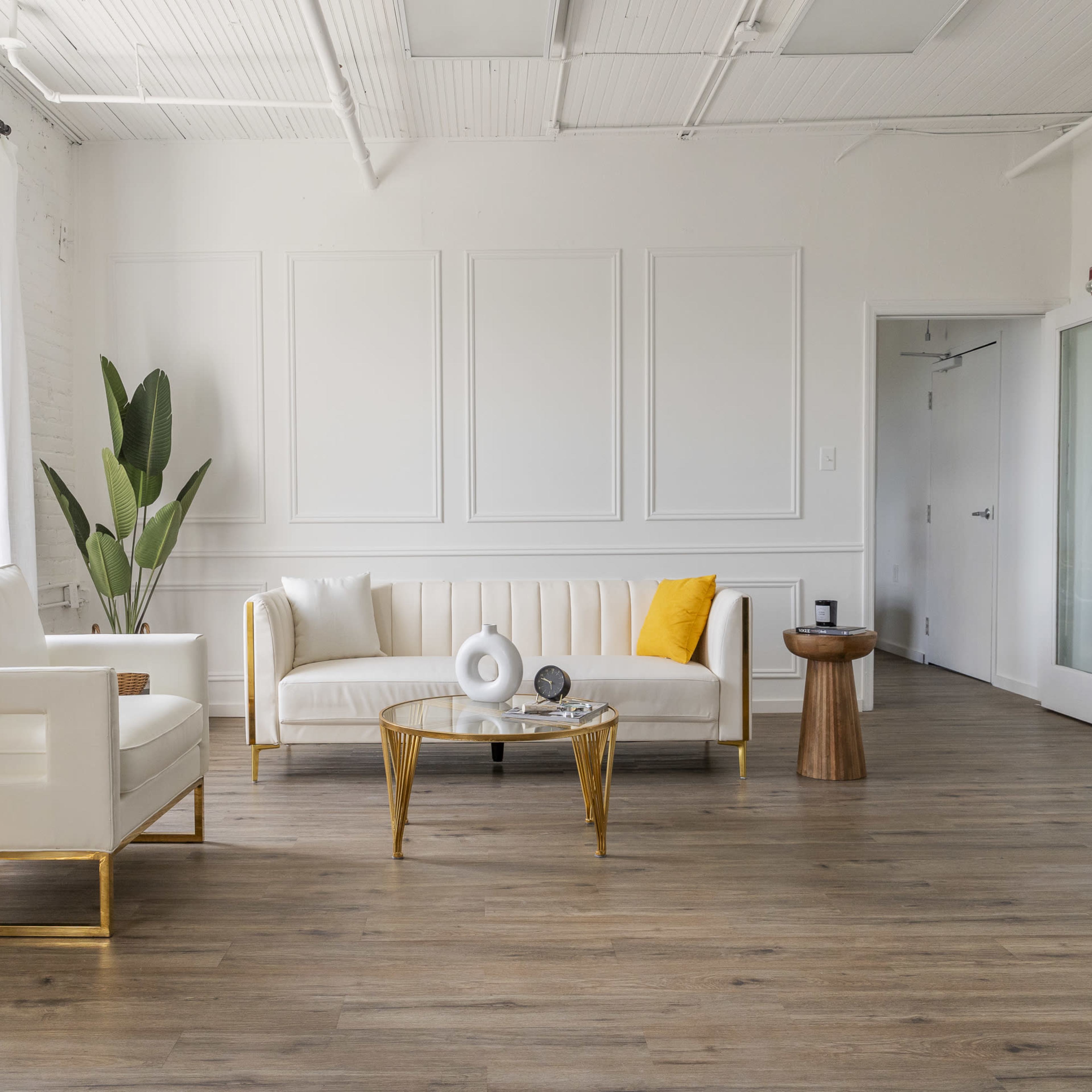 A modern, minimalist living room with a white sofa, a round coffee table, a yellow accent pillow, a plant, and a wooden side table.