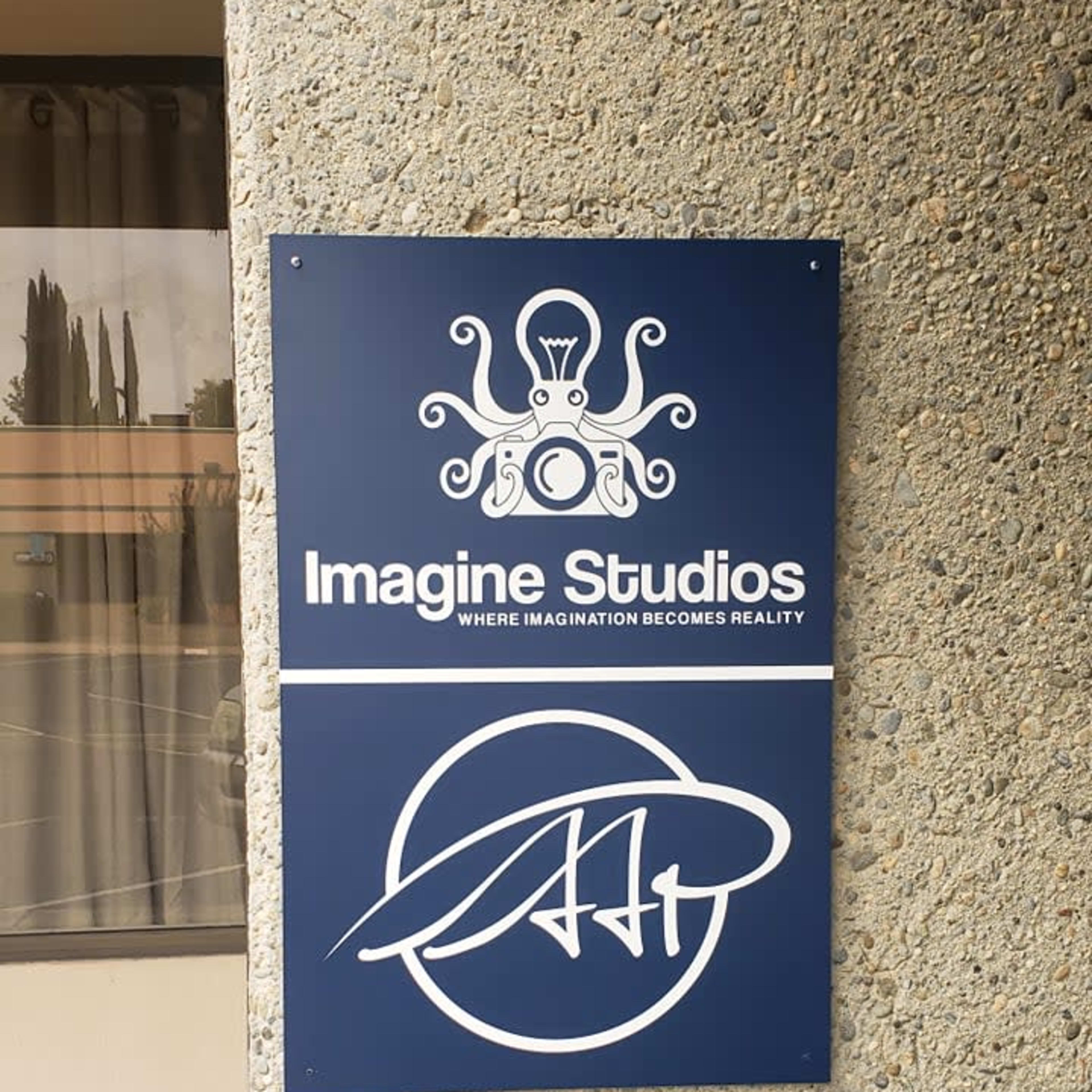 A sign for Imagine Studios featuring an octopus graphic and the tagline "WHERE IMAGINATION BECOMES REALITY" hangs on a textured gray wall.