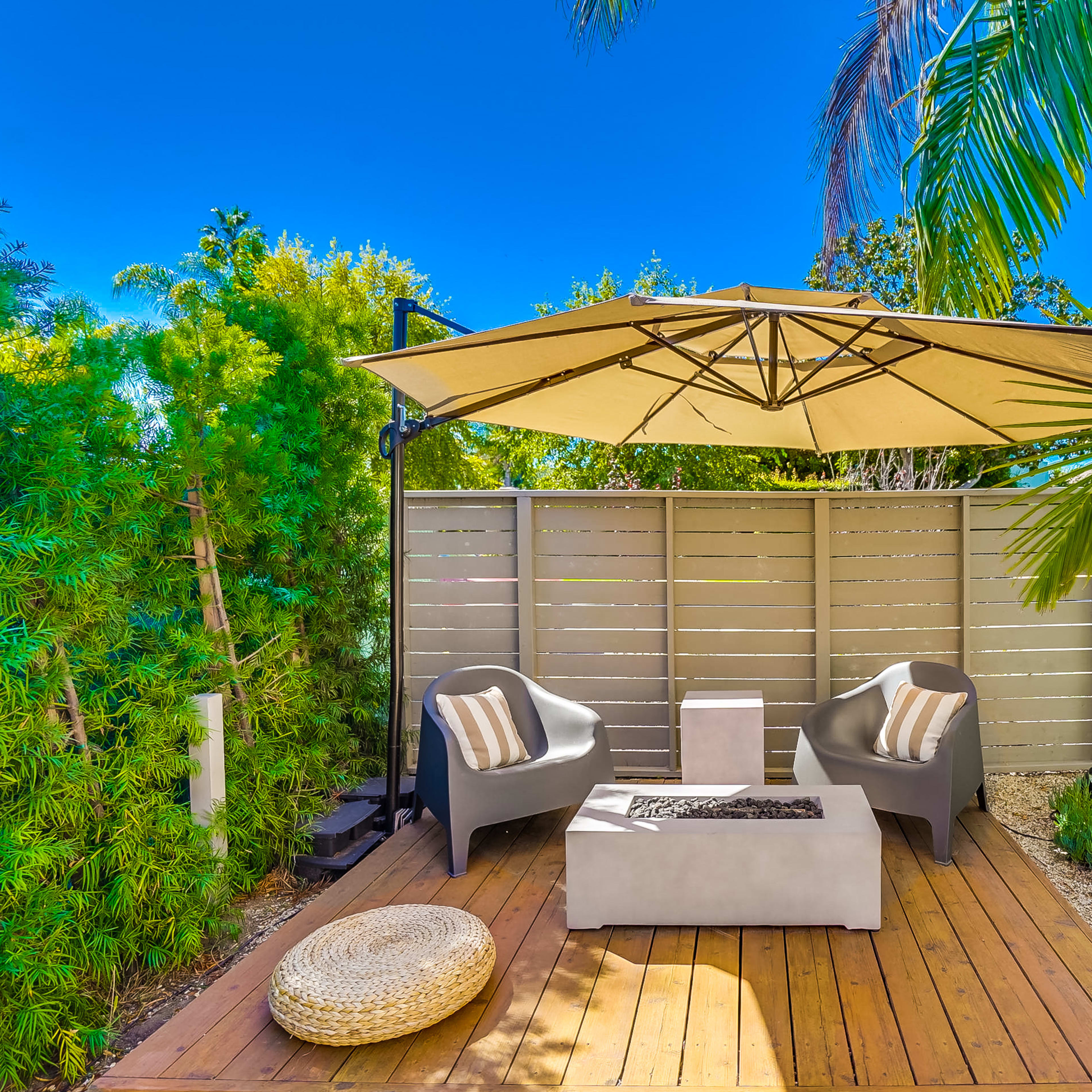 A small outdoor seating area features two chairs under a large umbrella with a coffee table and a surrounding garden.