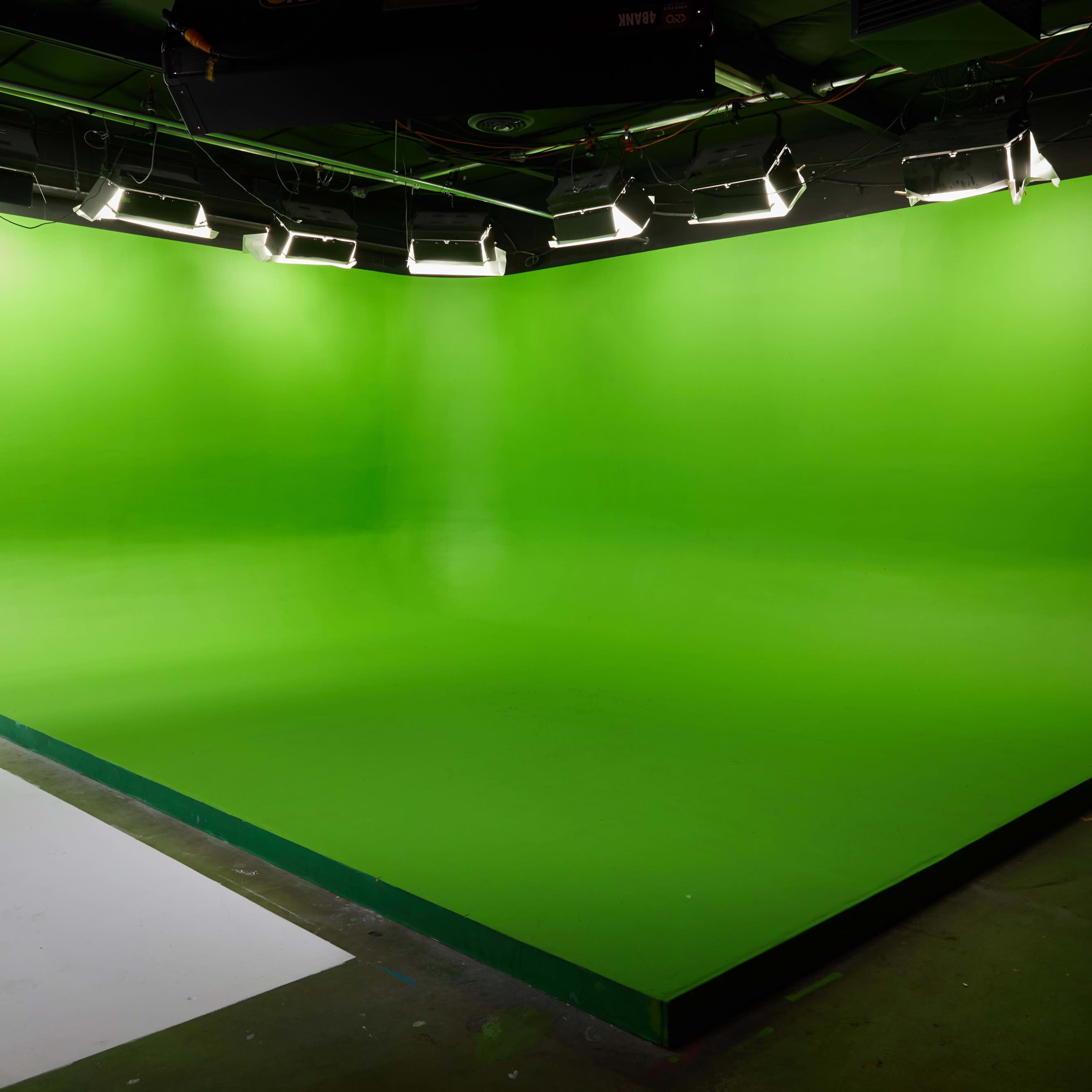 A green screen studio with uniform green walls and floor, equipped with overhead lights.