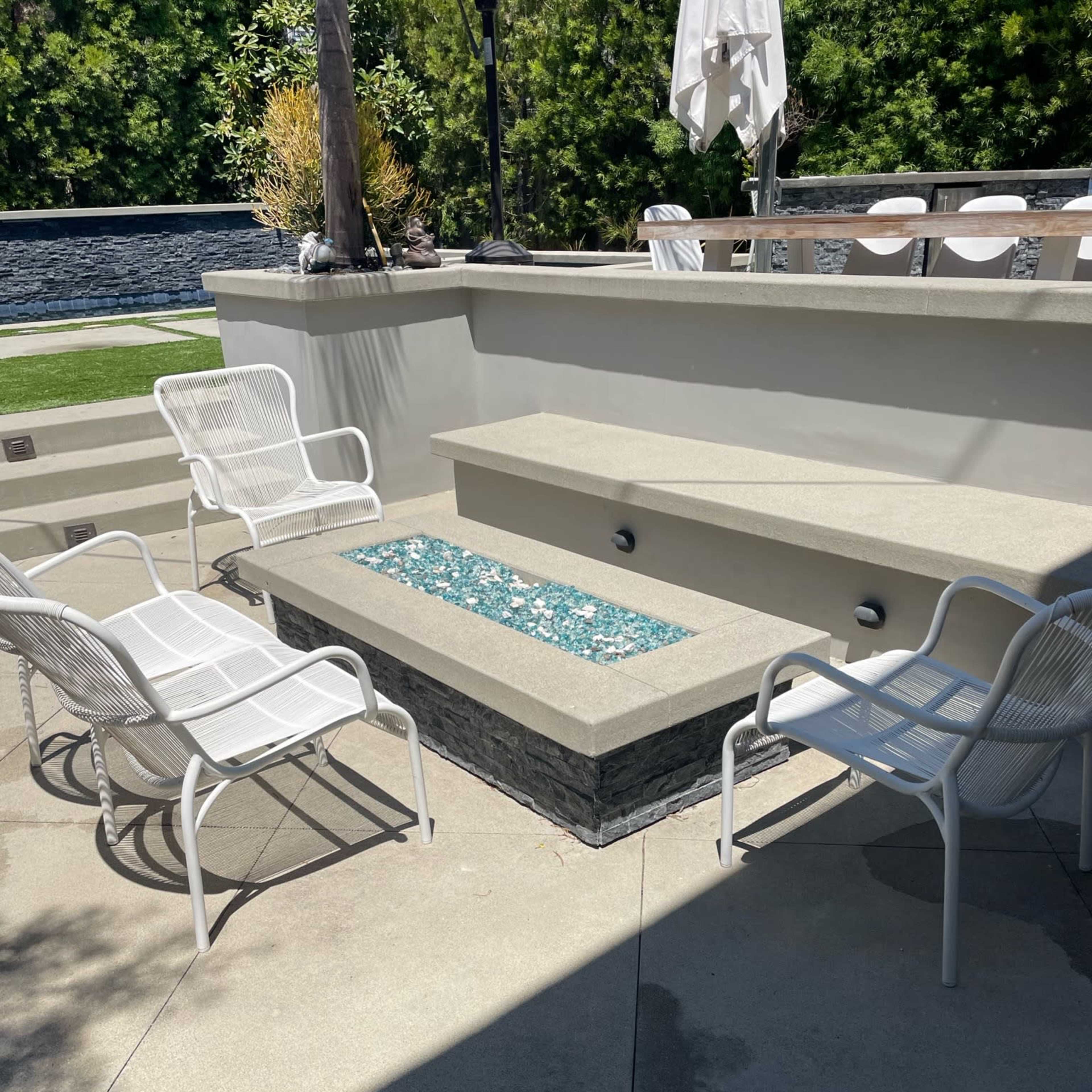 A sunlit outdoor seating area with white chairs arranged around a stone-accented platform featuring blue glass accents.