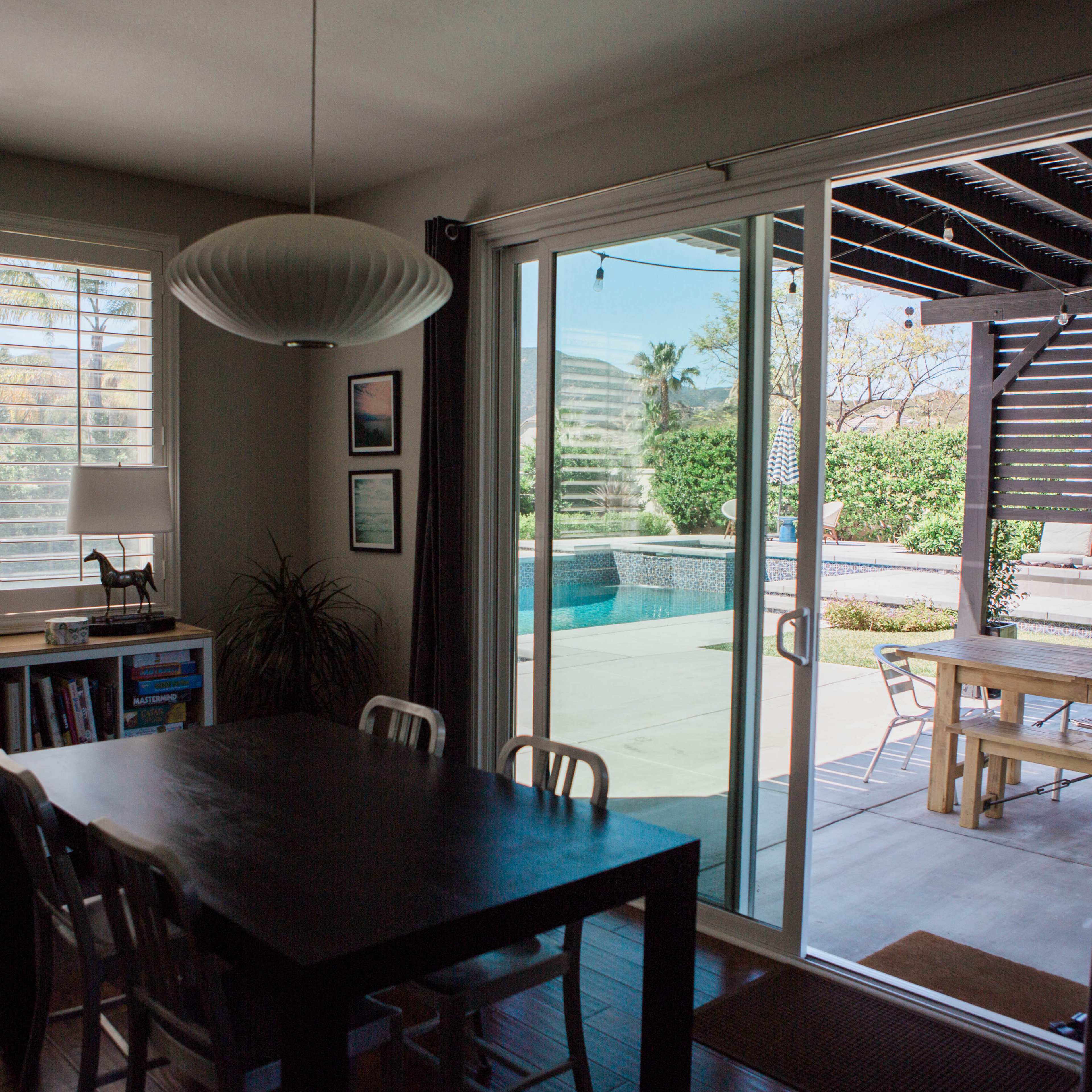 A dining area with a wooden table and chairs, leading to a patio and pool area through sliding glass doors.