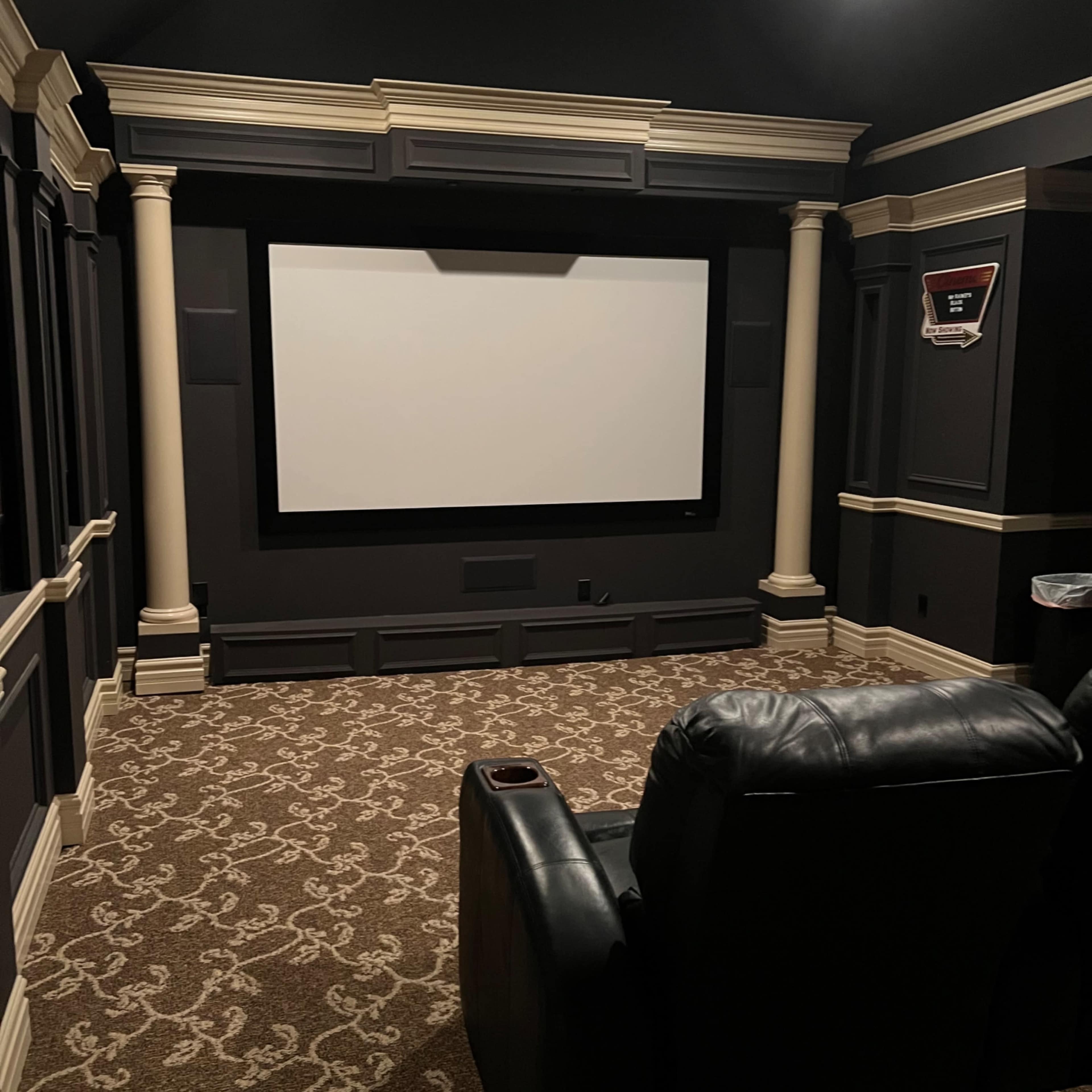 A home theater with a large screen at the front and a leather reclining chair positioned in front of it.