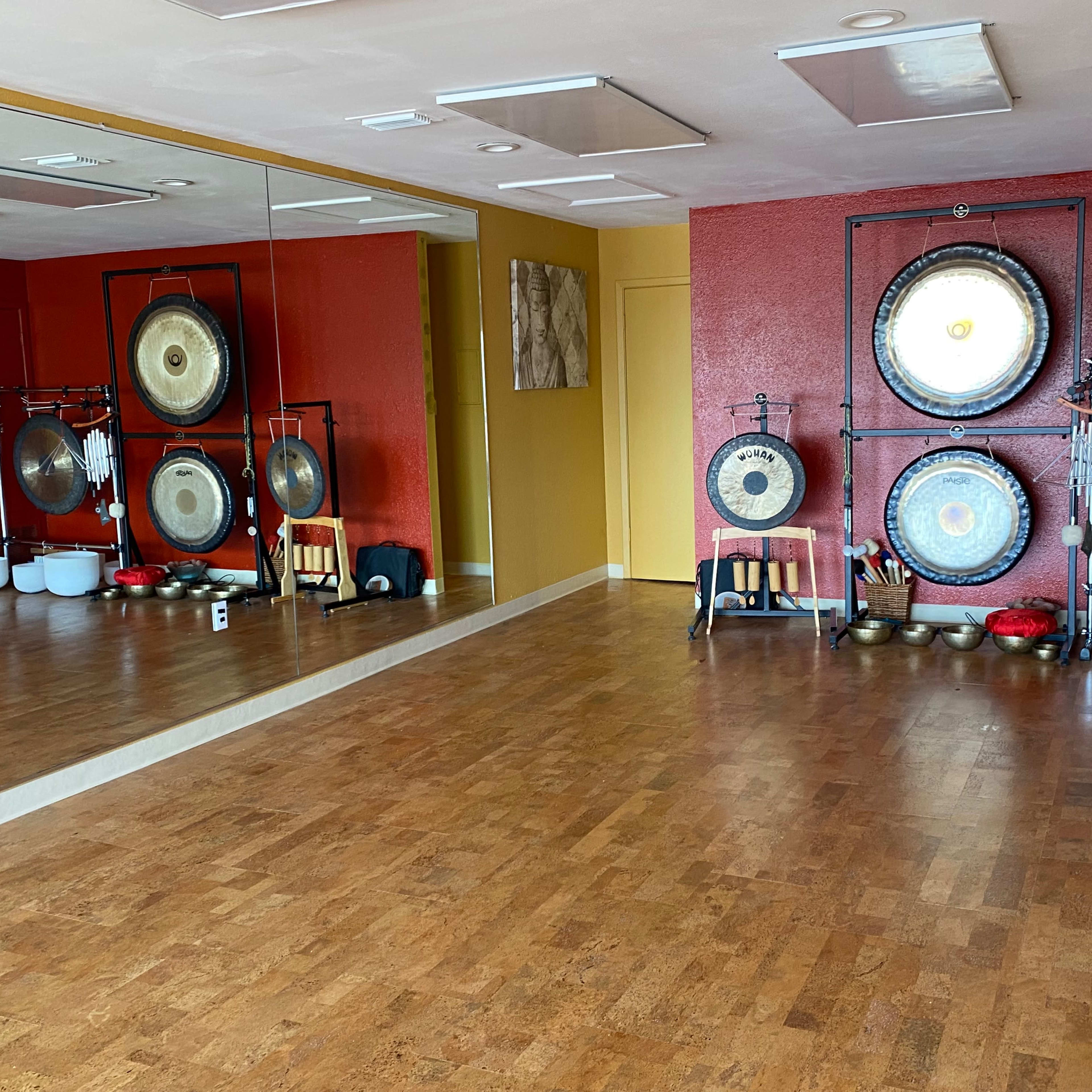 A spacious room with wooden floors and red walls, featuring a set of gongs and bowls arranged against a mirrored wall.