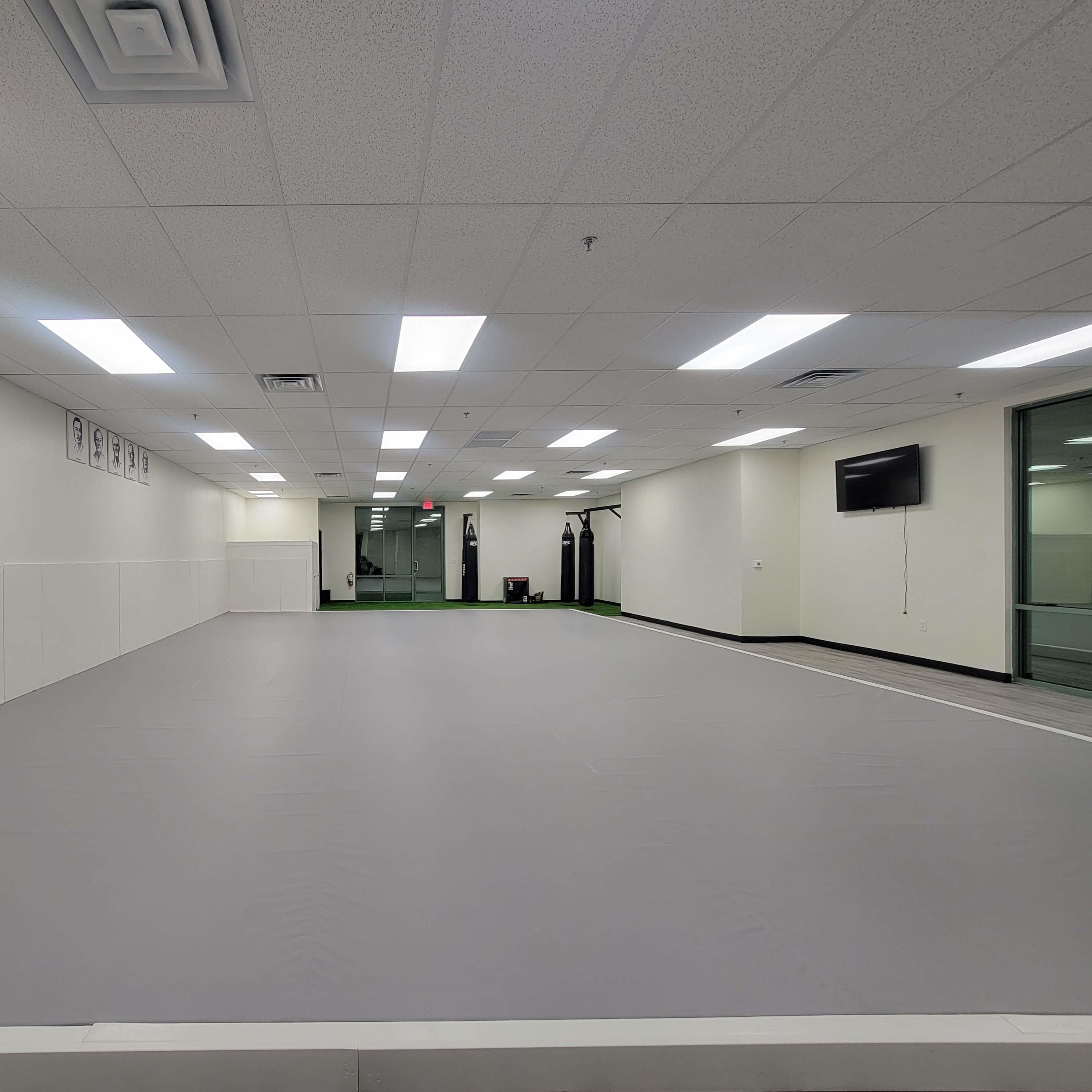 A spacious training room with gray flooring, white walls, and a few exercise equipment pieces in the background.