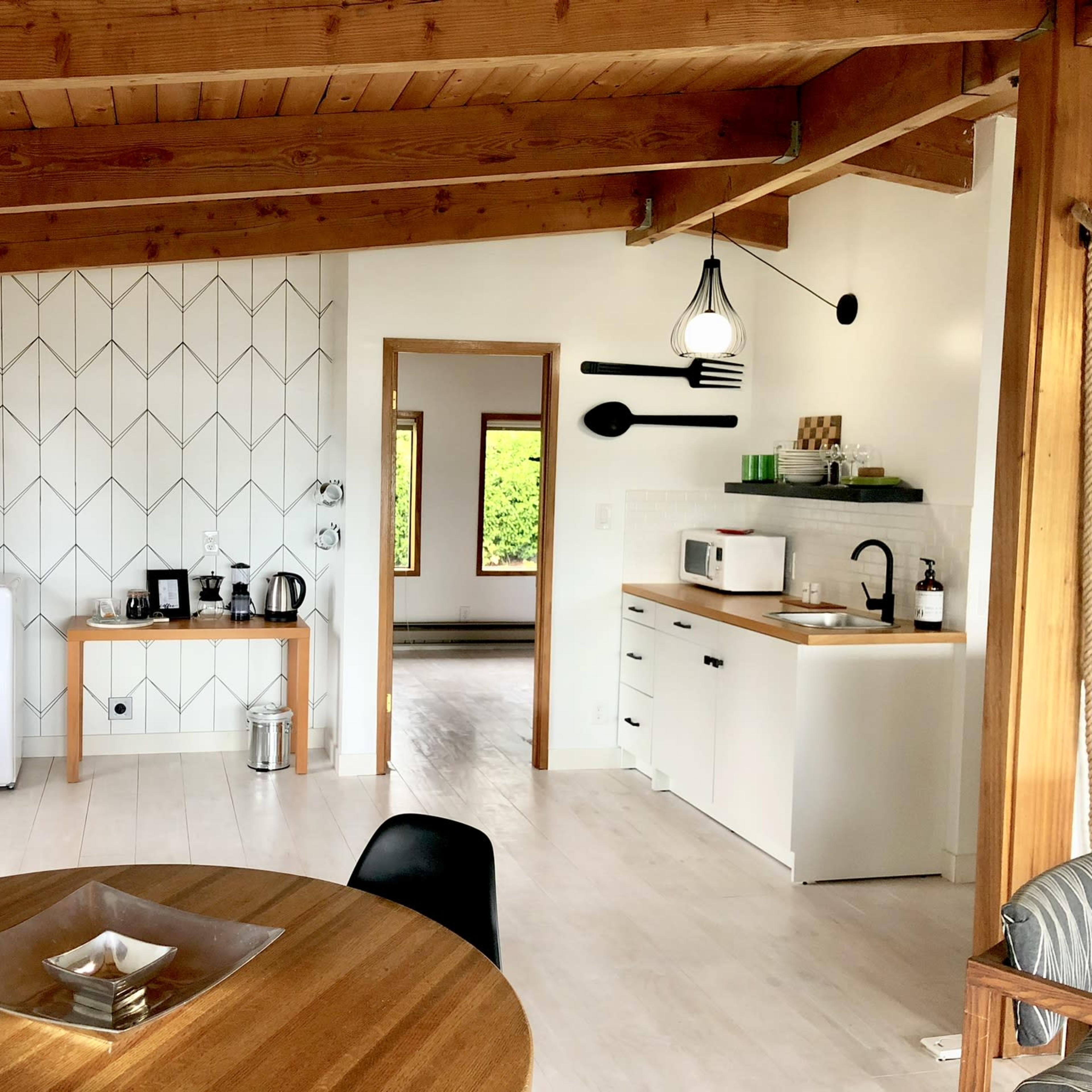 A modern, open-concept kitchen and dining area with wooden beams, a round dining table, and white cabinetry.