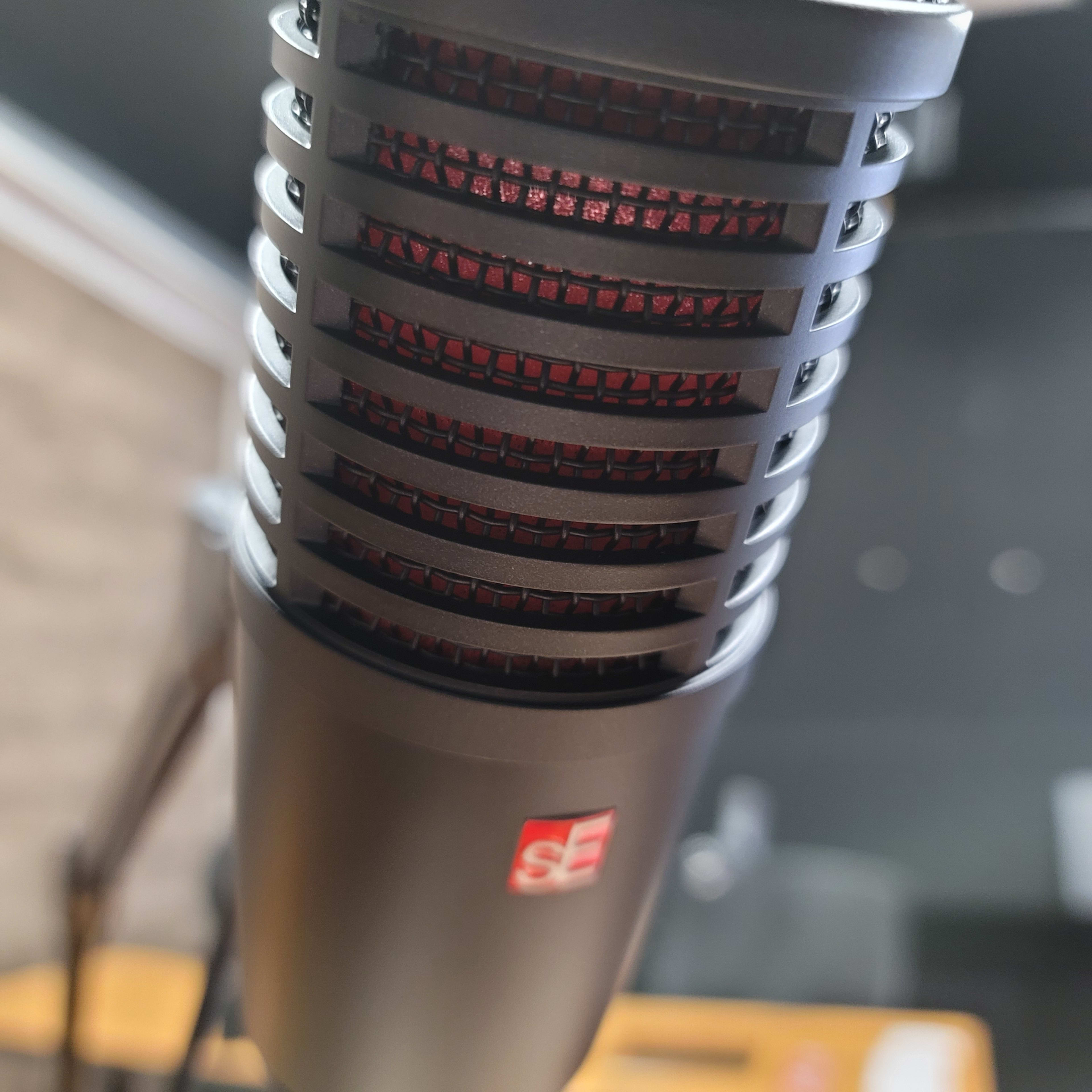 A close-up of a microphone with a black grill and red accents, placed on a wooden surface.