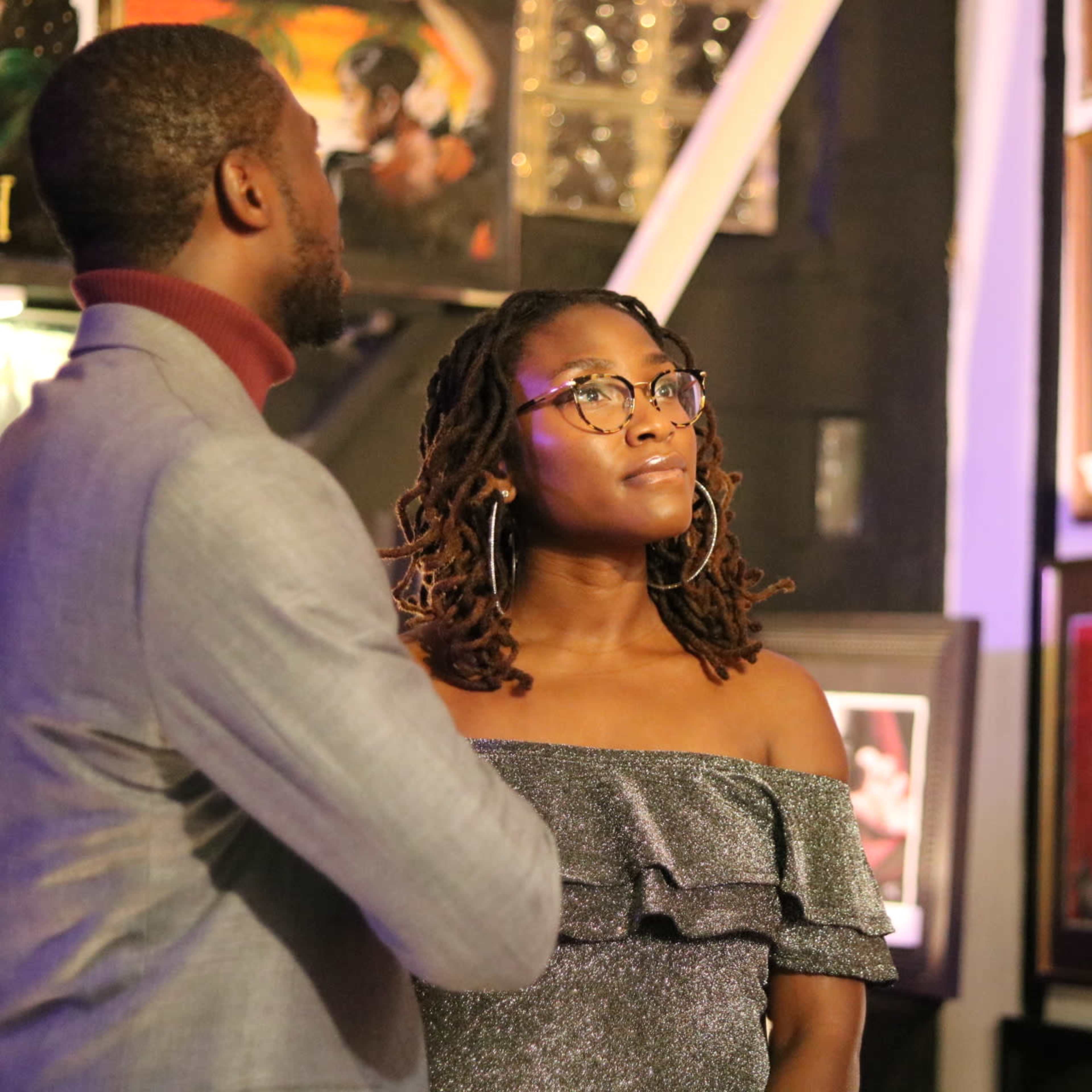 A man and a woman are looking at framed artwork on a gallery wall.