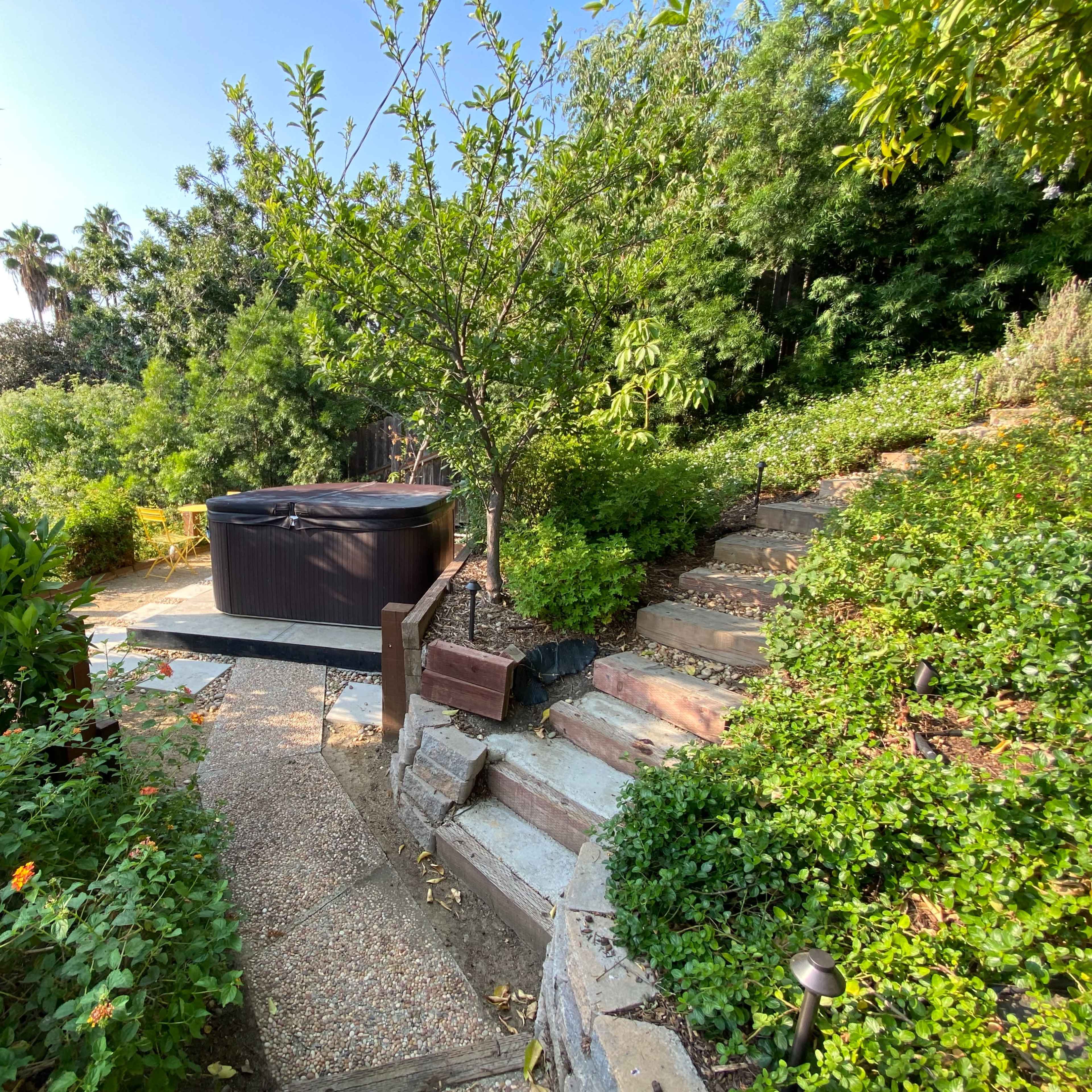 A hot tub is situated among lush greenery and stone steps in a landscaped garden.