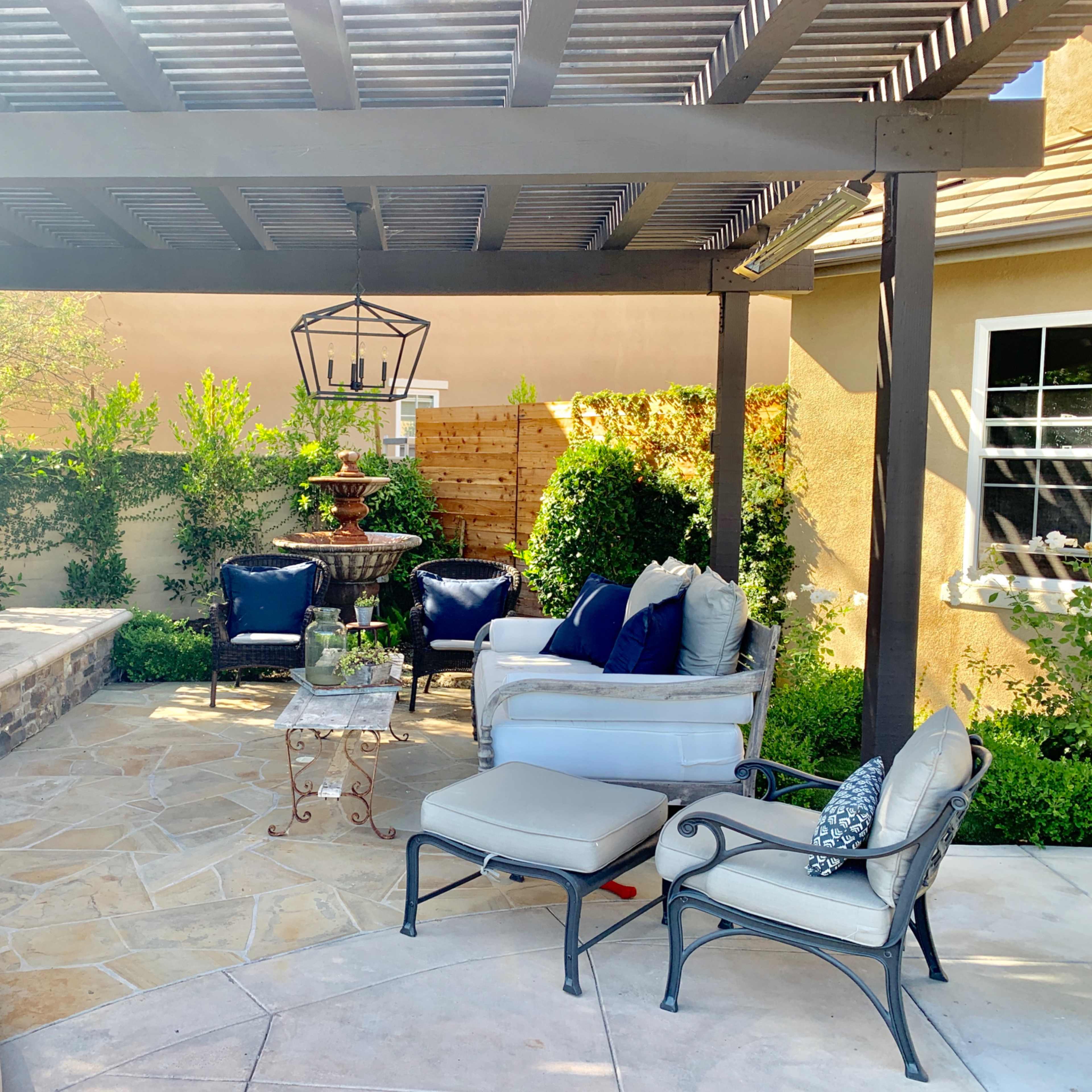A shaded patio area featuring comfortable seating, a stone fireplace, and decorative plants.
