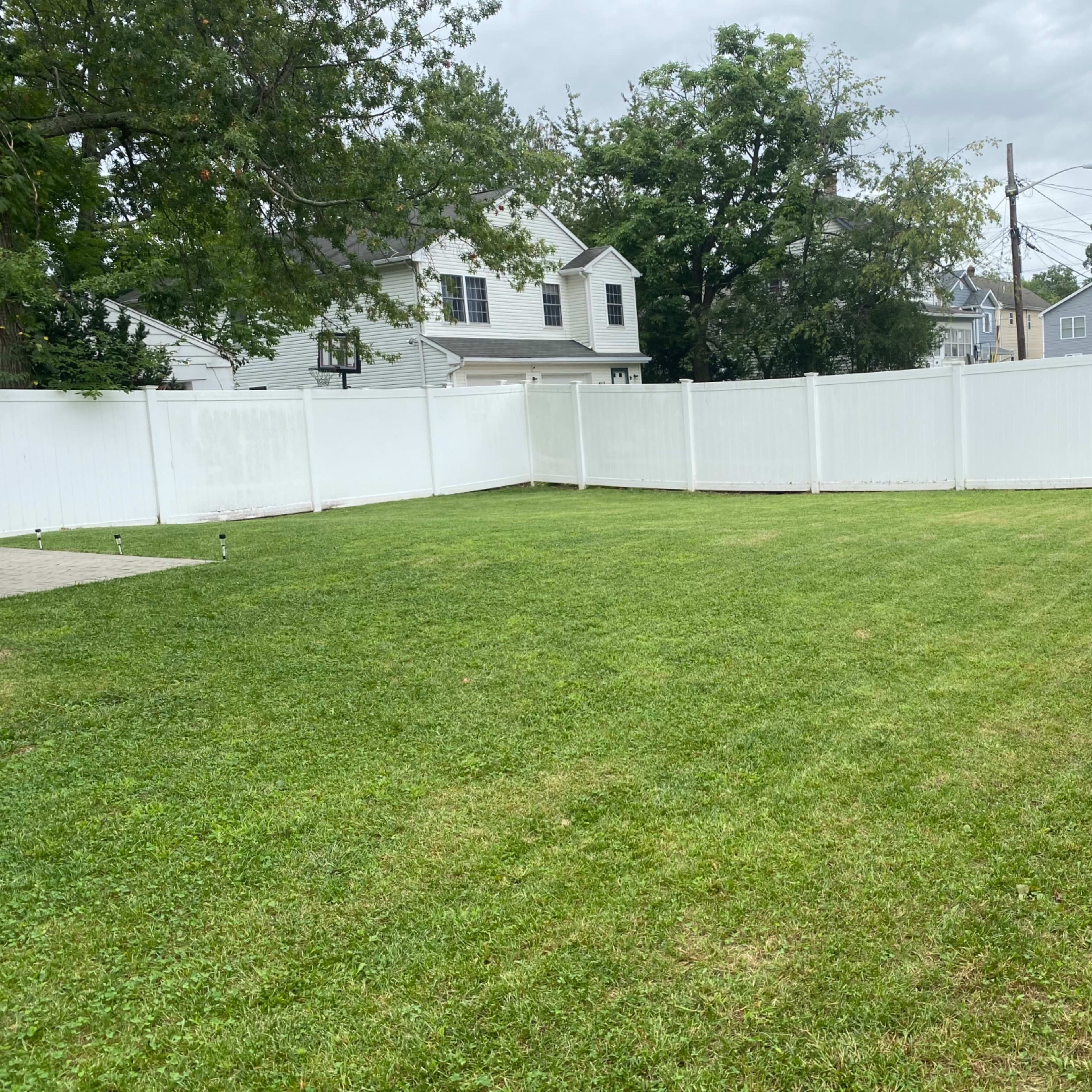 A spacious, neatly mowed backyard enclosed by a white vinyl fence.