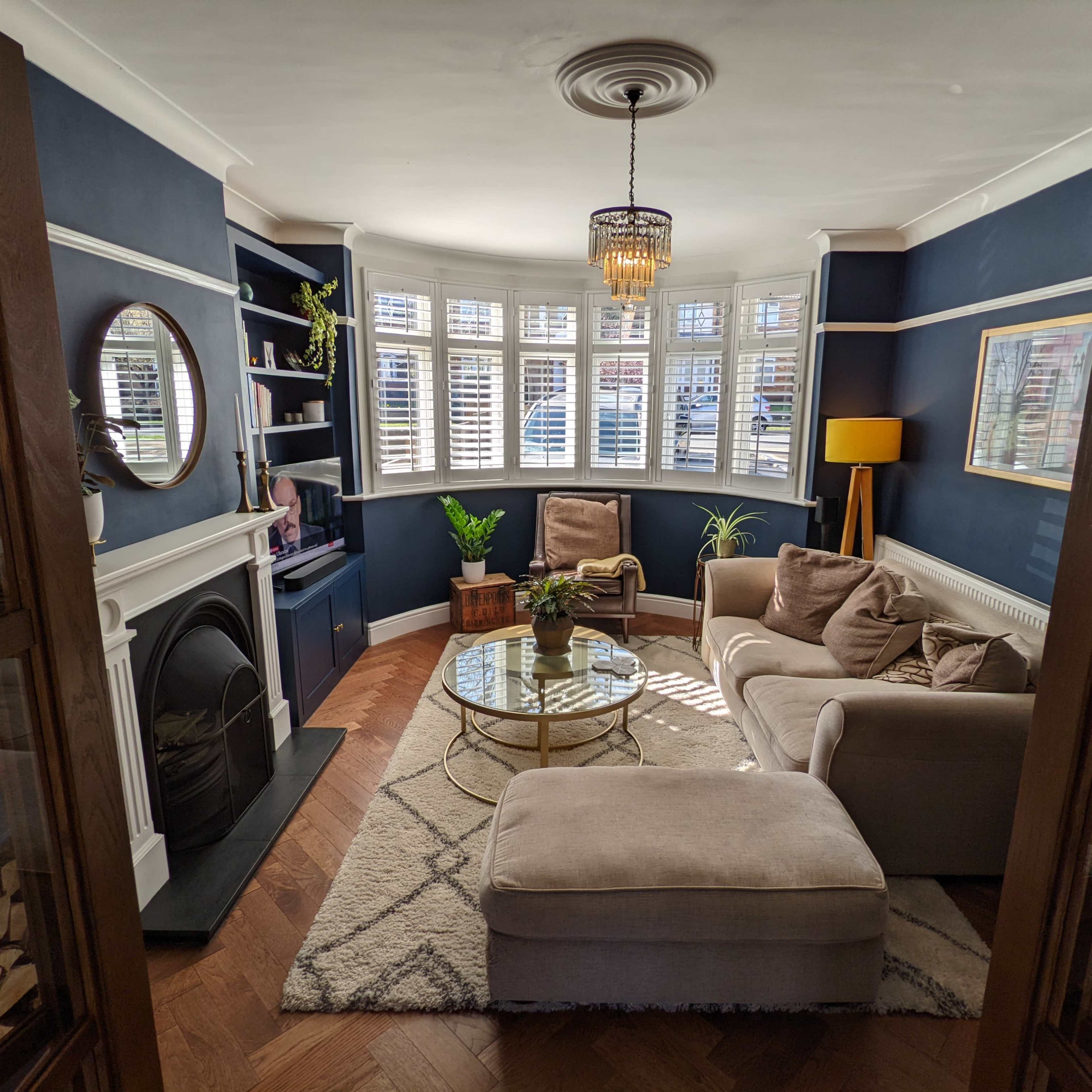 A cozy living room features a circular coffee table, two armchairs, and a decorative lamp, with large windows allowing natural light to illuminate the space.