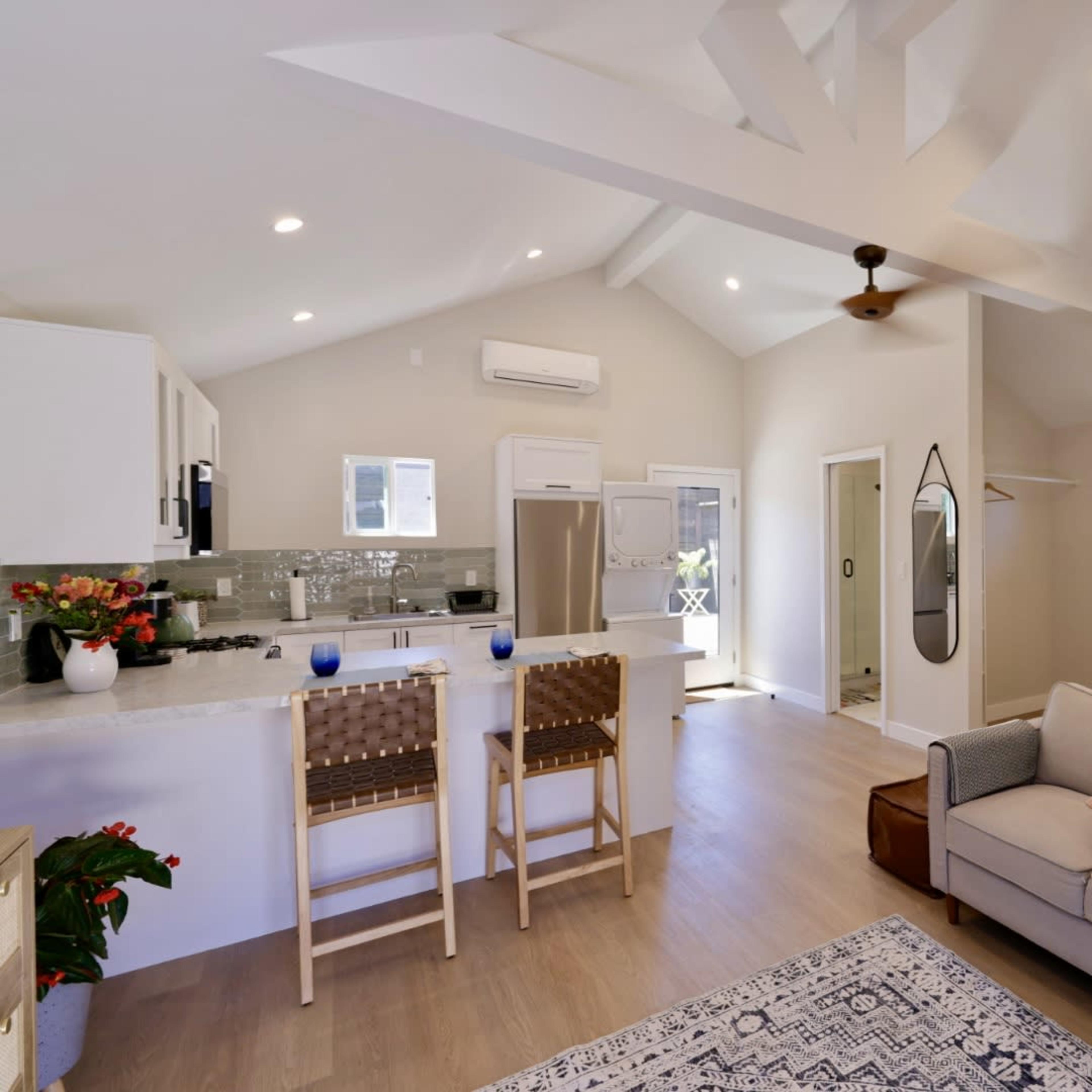 A modern, open-concept living space with a kitchen, a seating area, and a bedroom area featuring a large window and sliding doors.