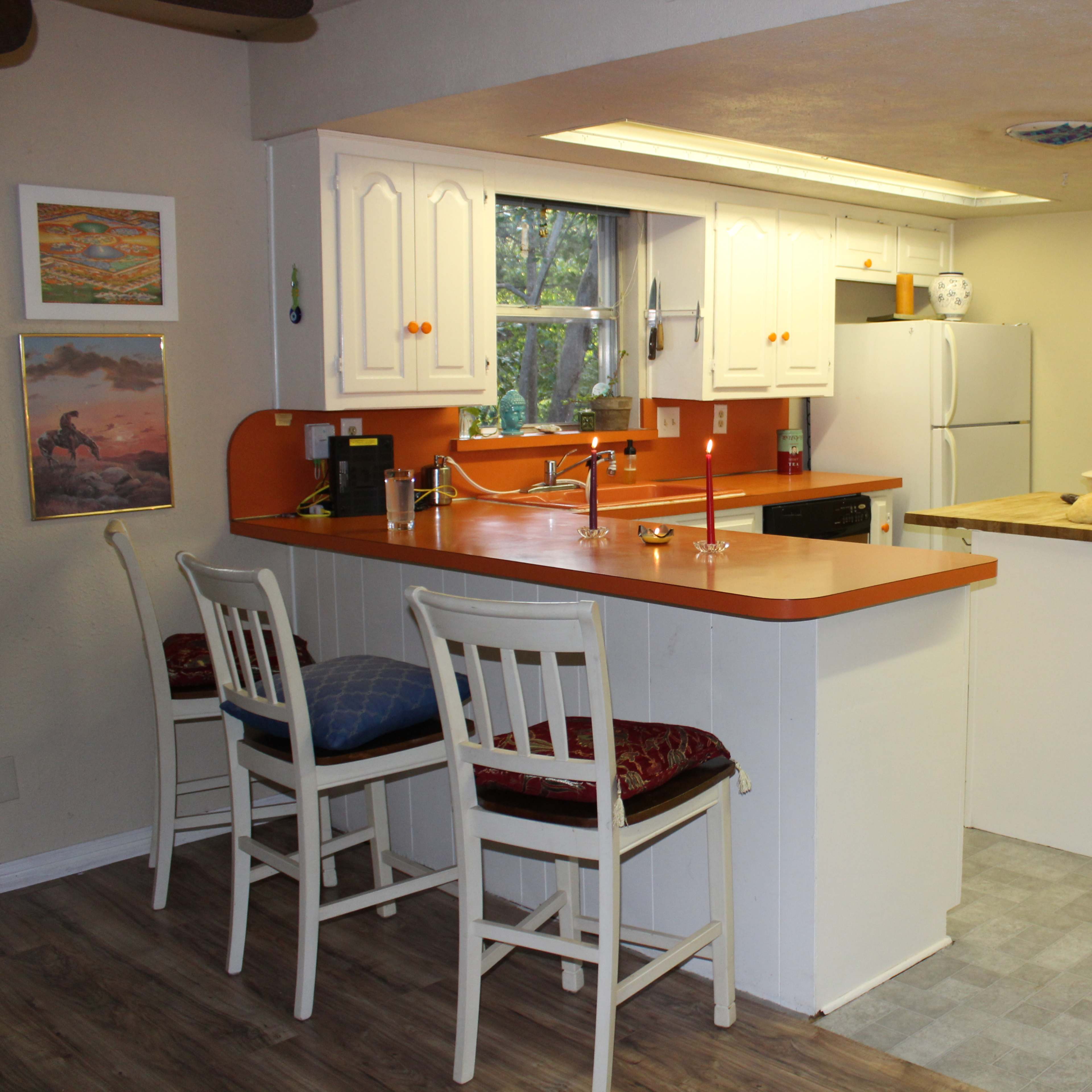 A kitchen featuring white cabinetry with orange countertops, a central island, and bar seating.