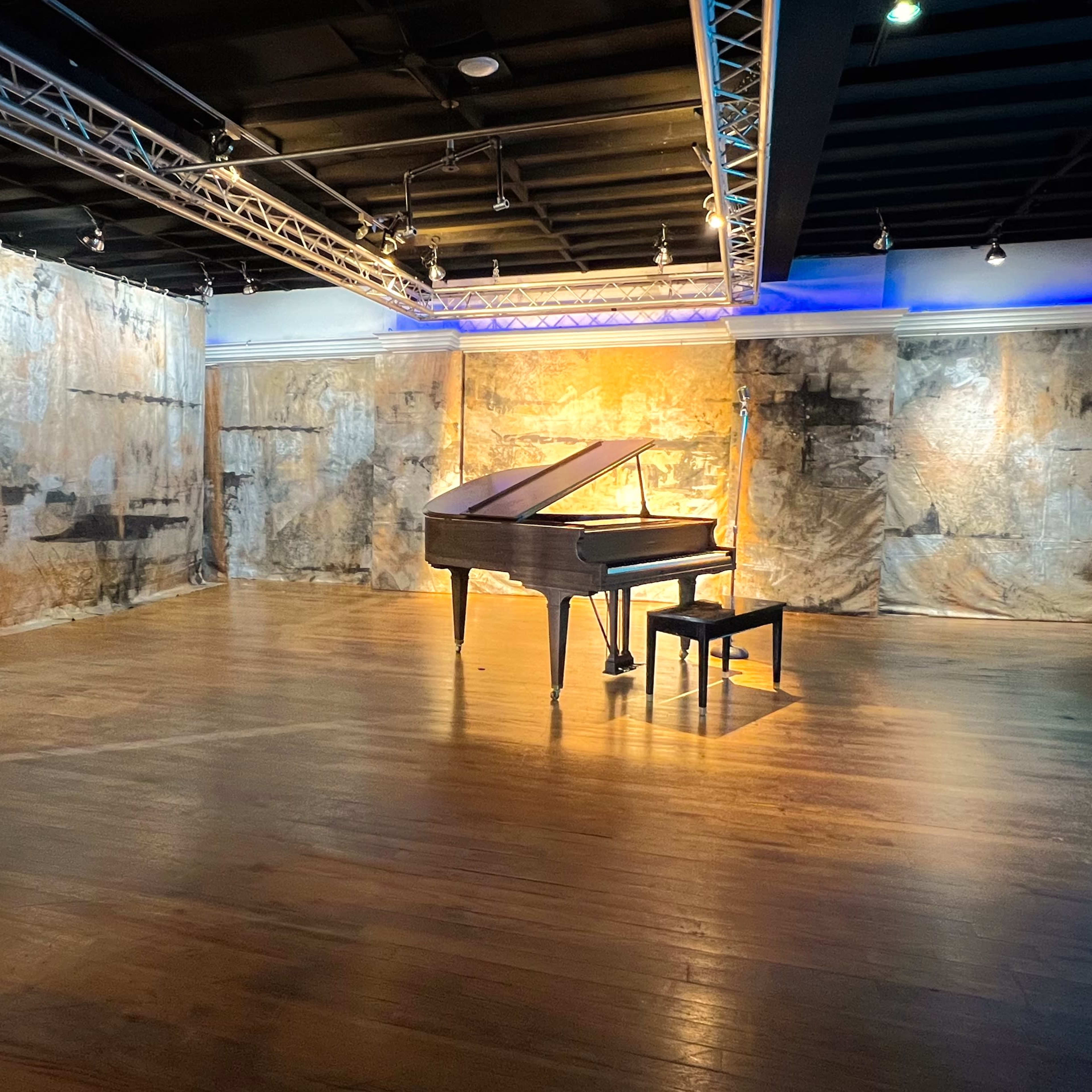 A grand piano sits alone in the center of a spacious room with textured, painted walls and wooden flooring.