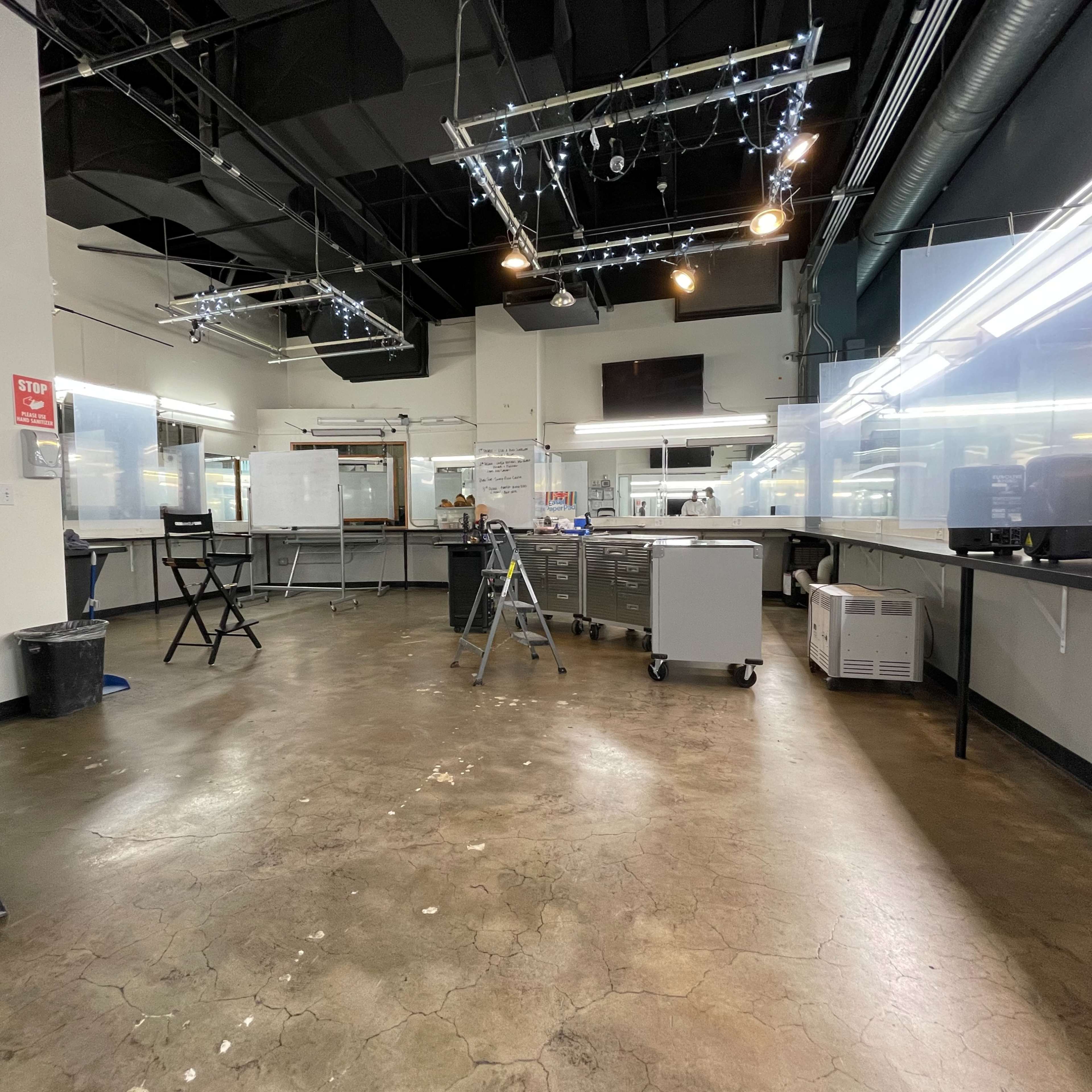 An empty workspace with several workstations, a ladder, and transparent partitions set up around the area.