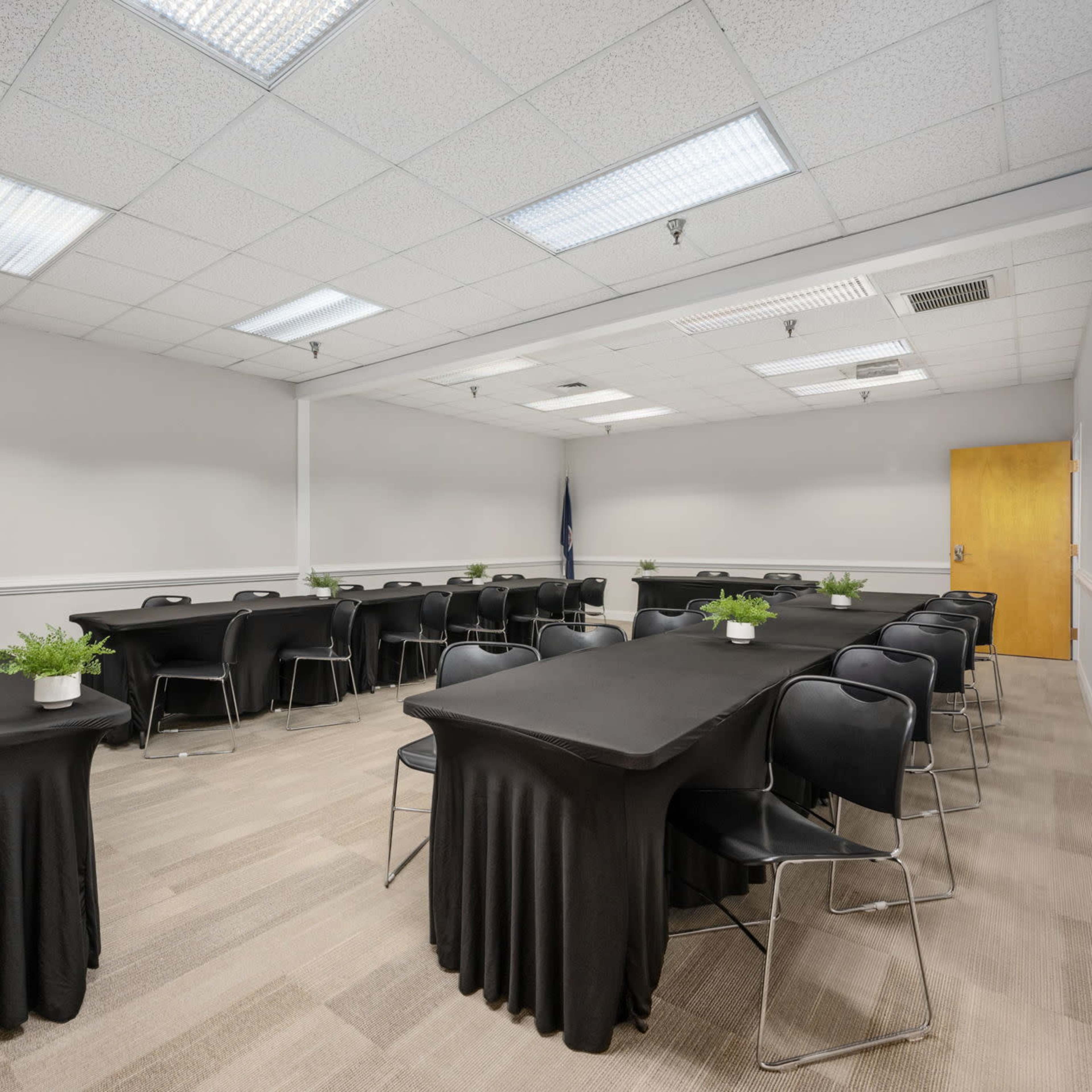 A conference room arranged with multiple tables covered in black cloth and black chairs, with a podium in one corner and a door at the back.