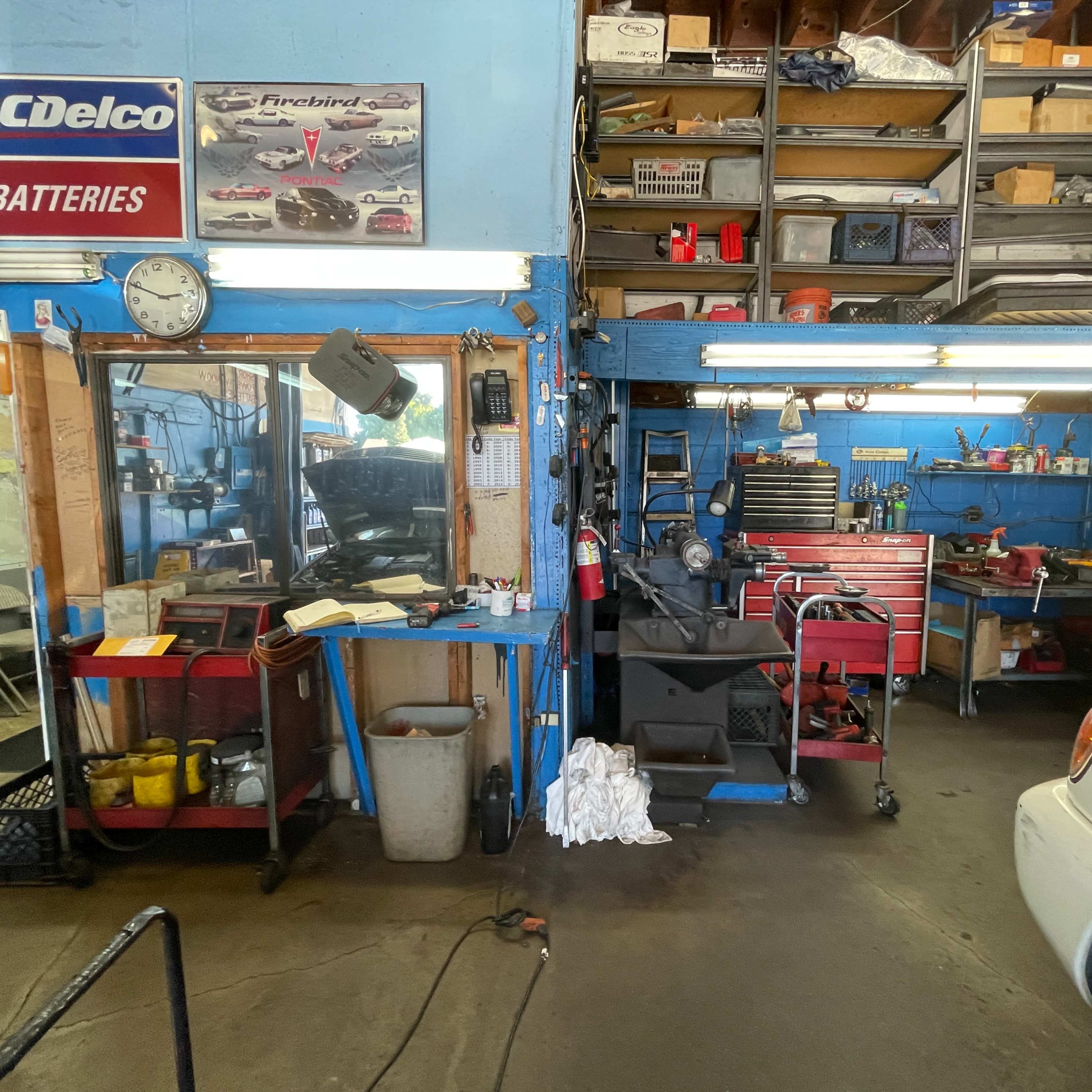 A mechanic's workshop featuring a workbench with tools, cabinets filled with equipment, and a white vehicle parked on a concrete floor.