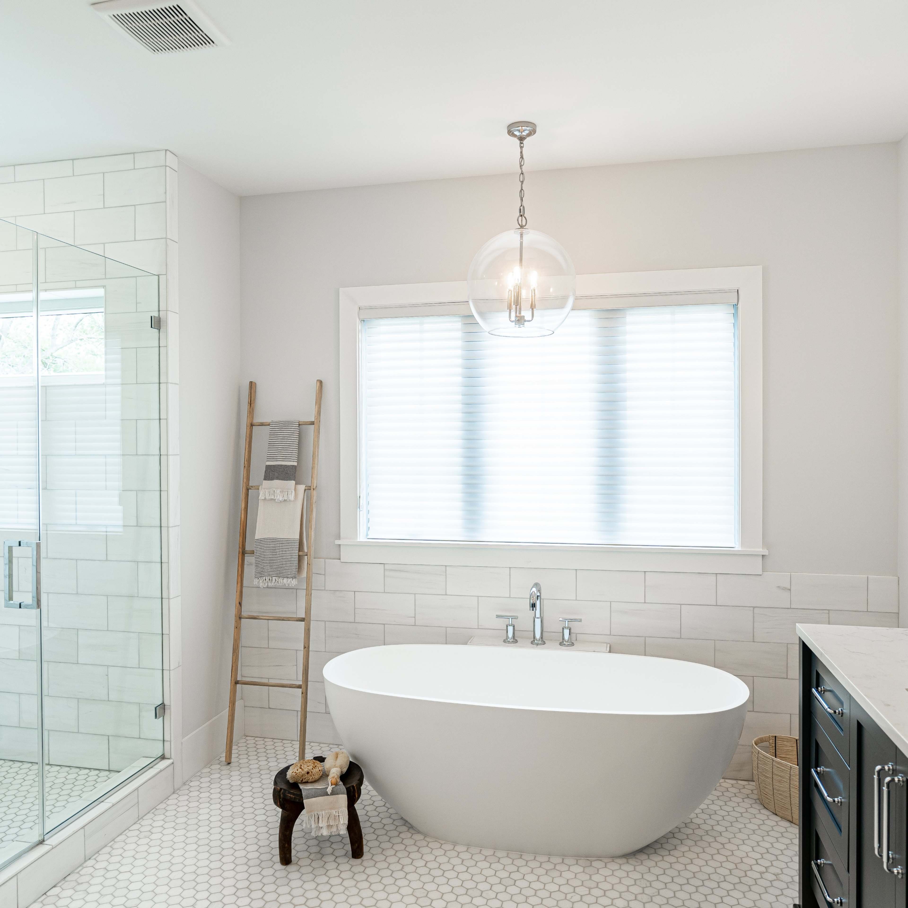A modern bathroom featuring a freestanding bathtub, a glass-enclosed shower, and a double sink vanity, all complemented by large windows allowing natural light.