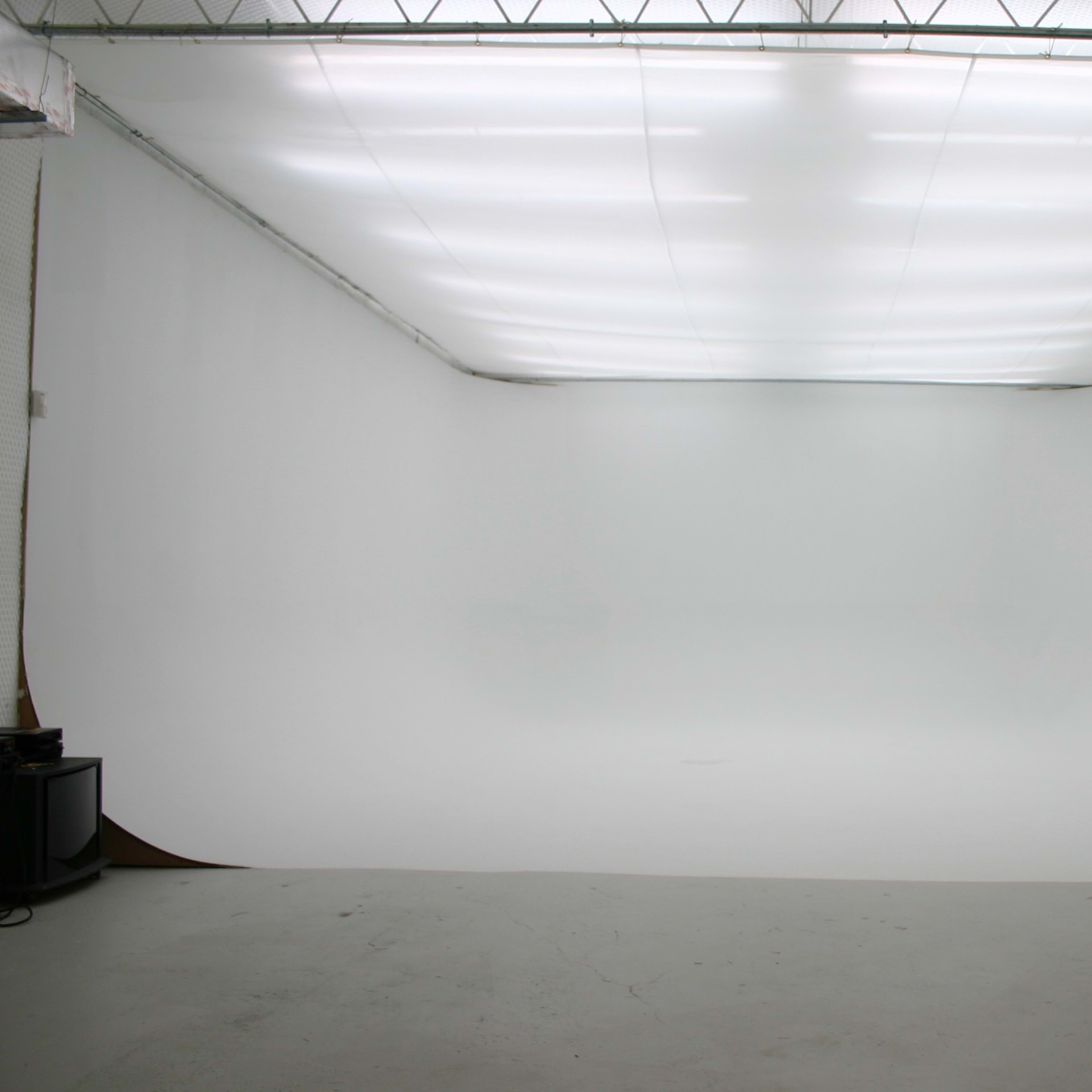 A large, empty studio space features a seamless white backdrop and bright overhead lighting.
