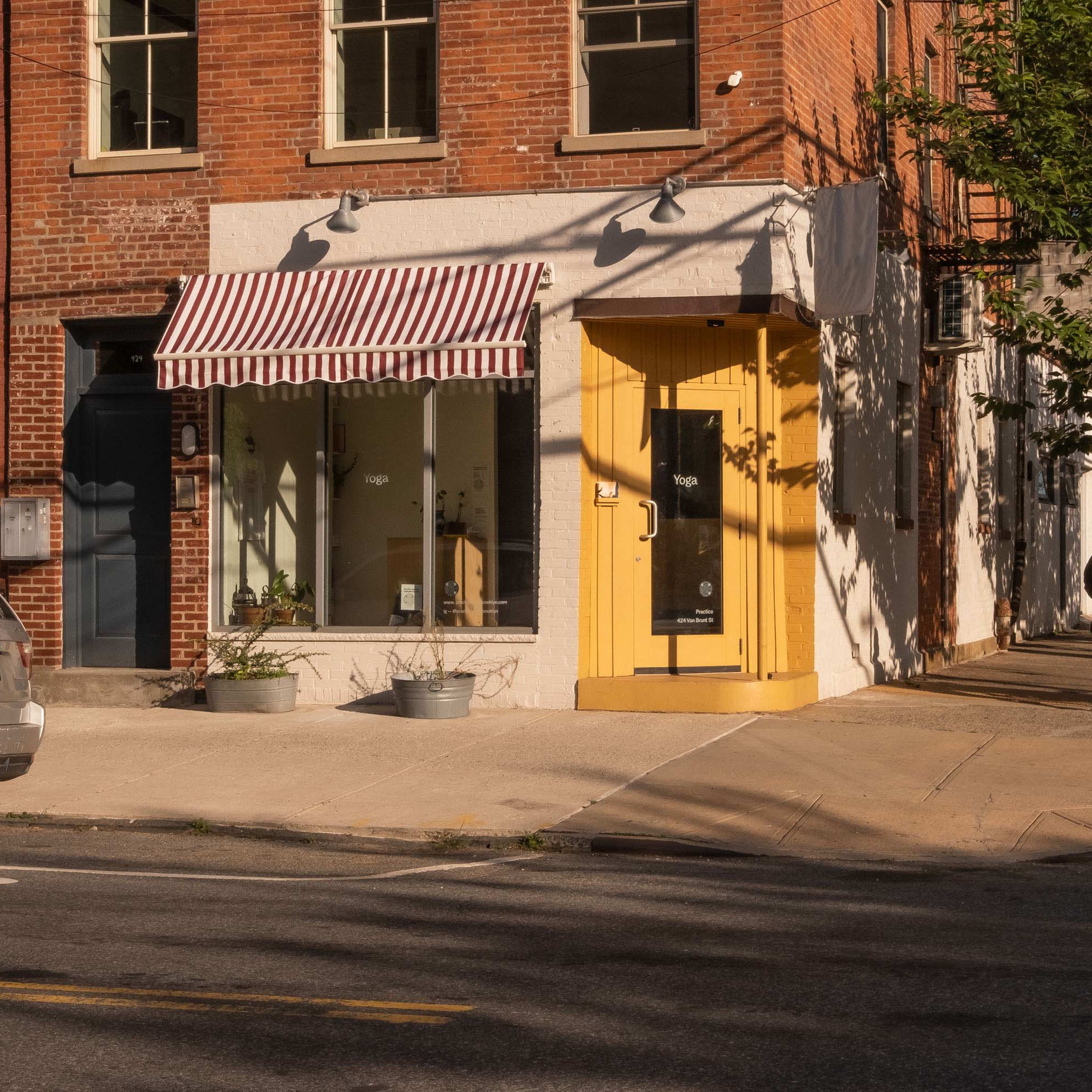 A gray SUV is parked on the street in front of a brick building with a yellow door and a shop window featuring an awning.