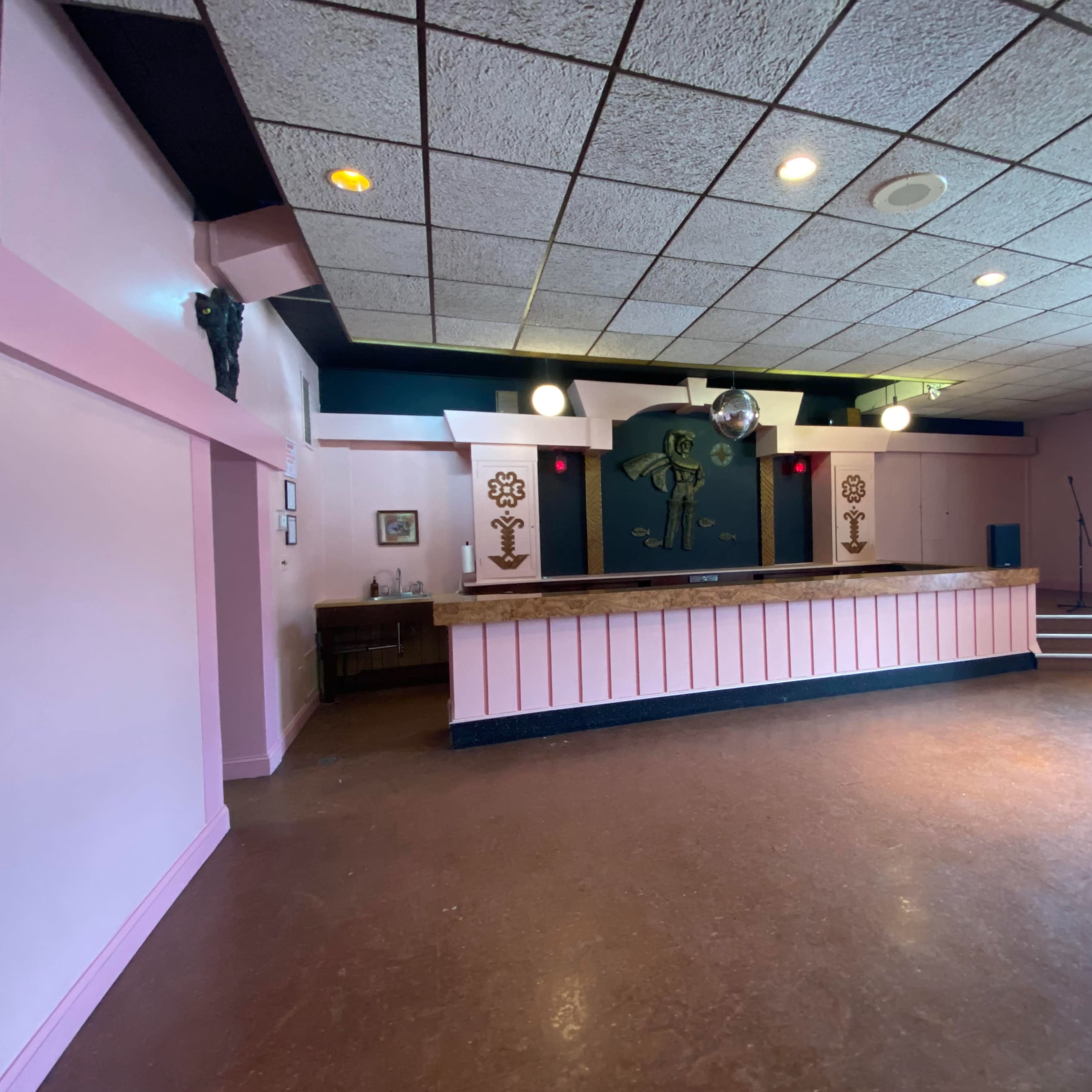 A vacant reception area with a pink-painted wall, a counter, and a small stage in the background.
