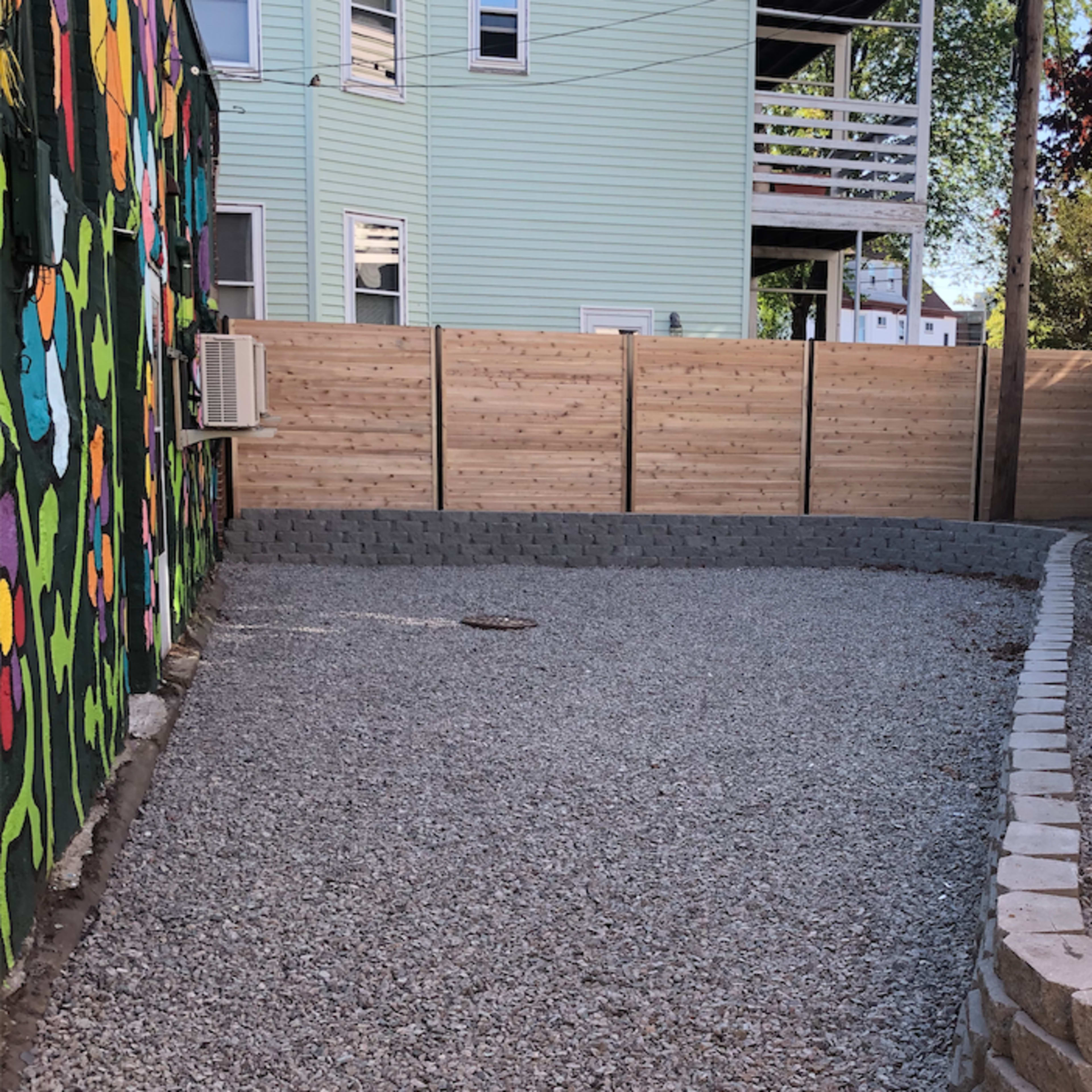 A gravel area enclosed by wooden fencing, with a colorful mural visible on one side.