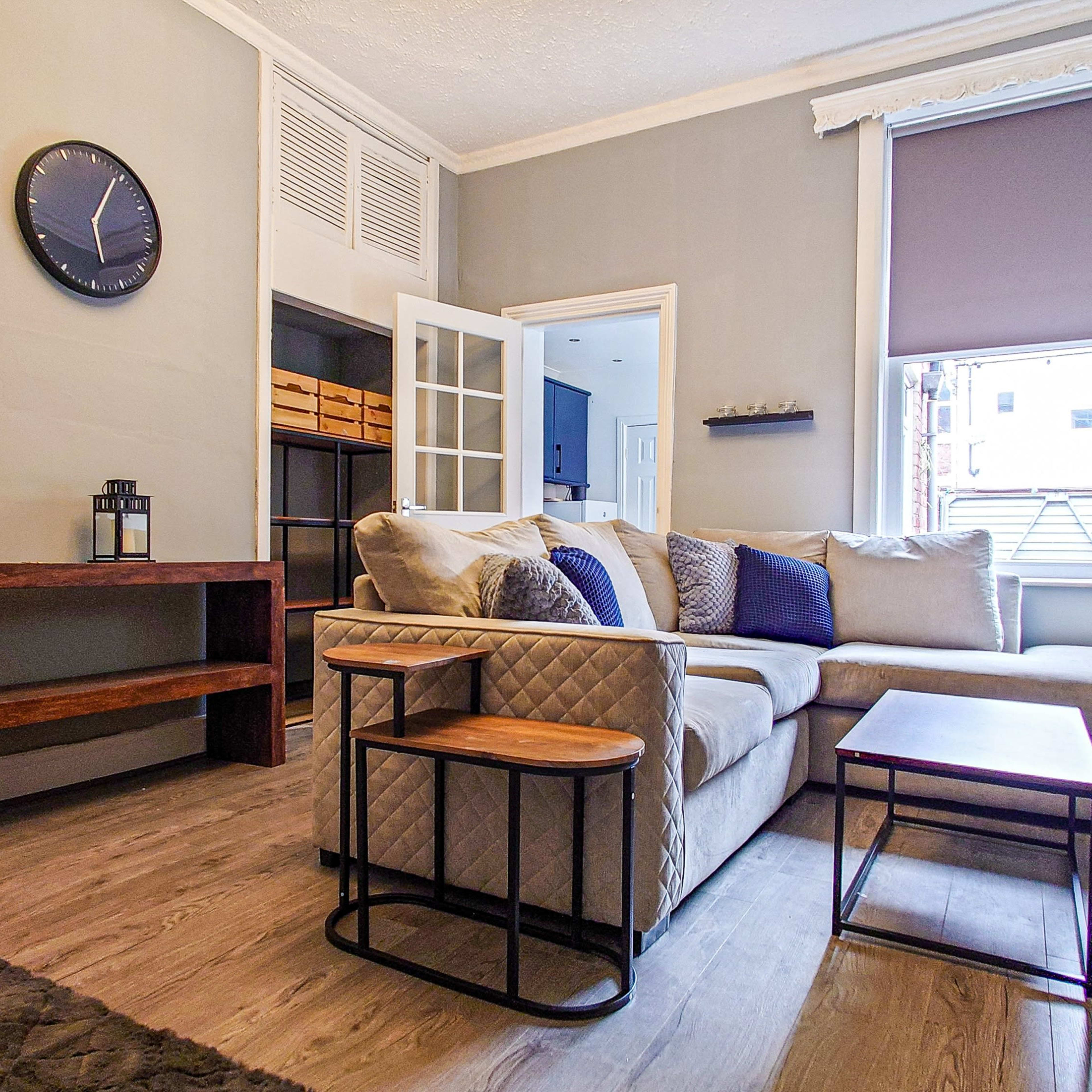A small living room with a beige sectional sofa, a wooden coffee table, and a wall-mounted television beside a window.