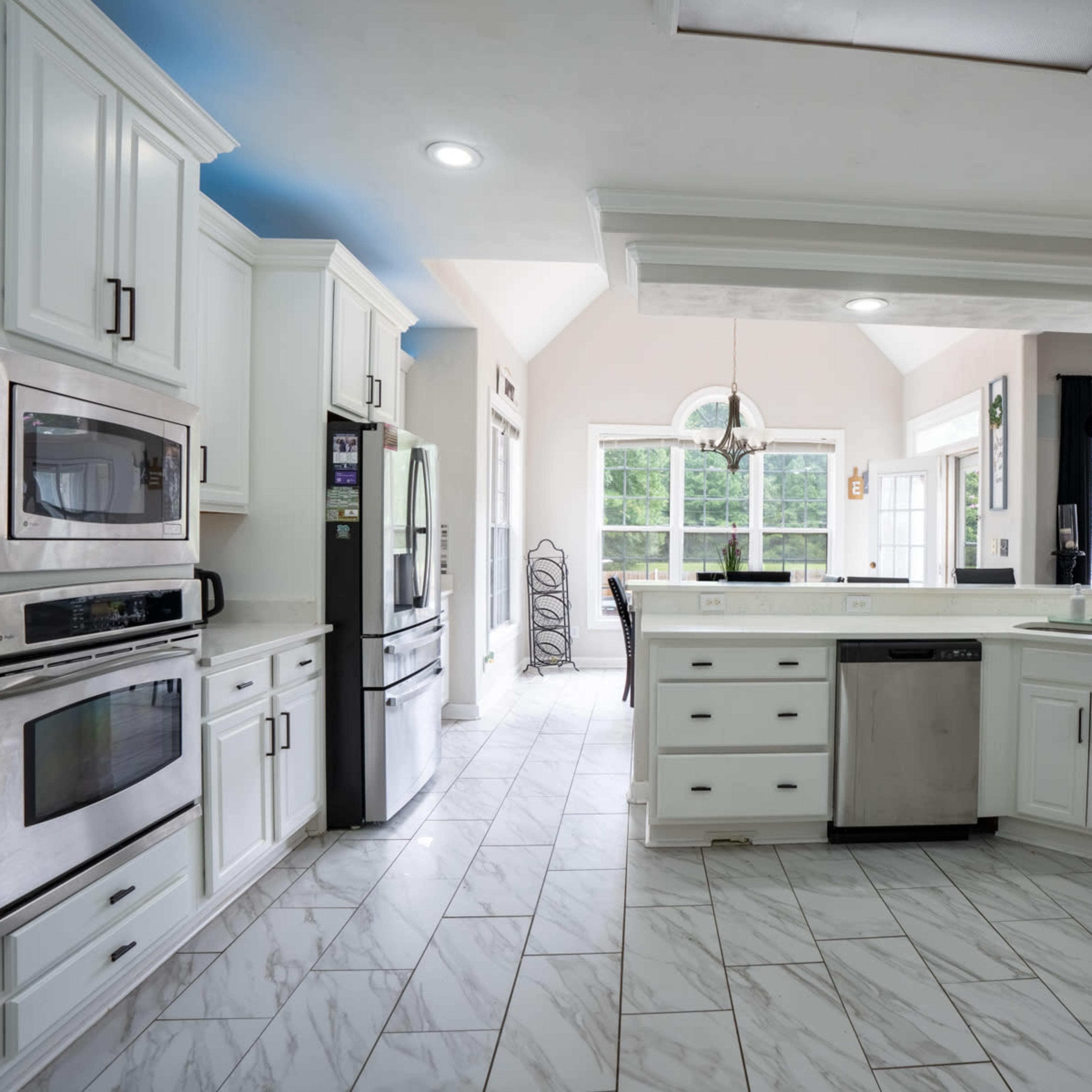 A modern kitchen featuring white cabinets, stainless steel appliances, and a large central island with a sink, set in a bright and spacious layout.