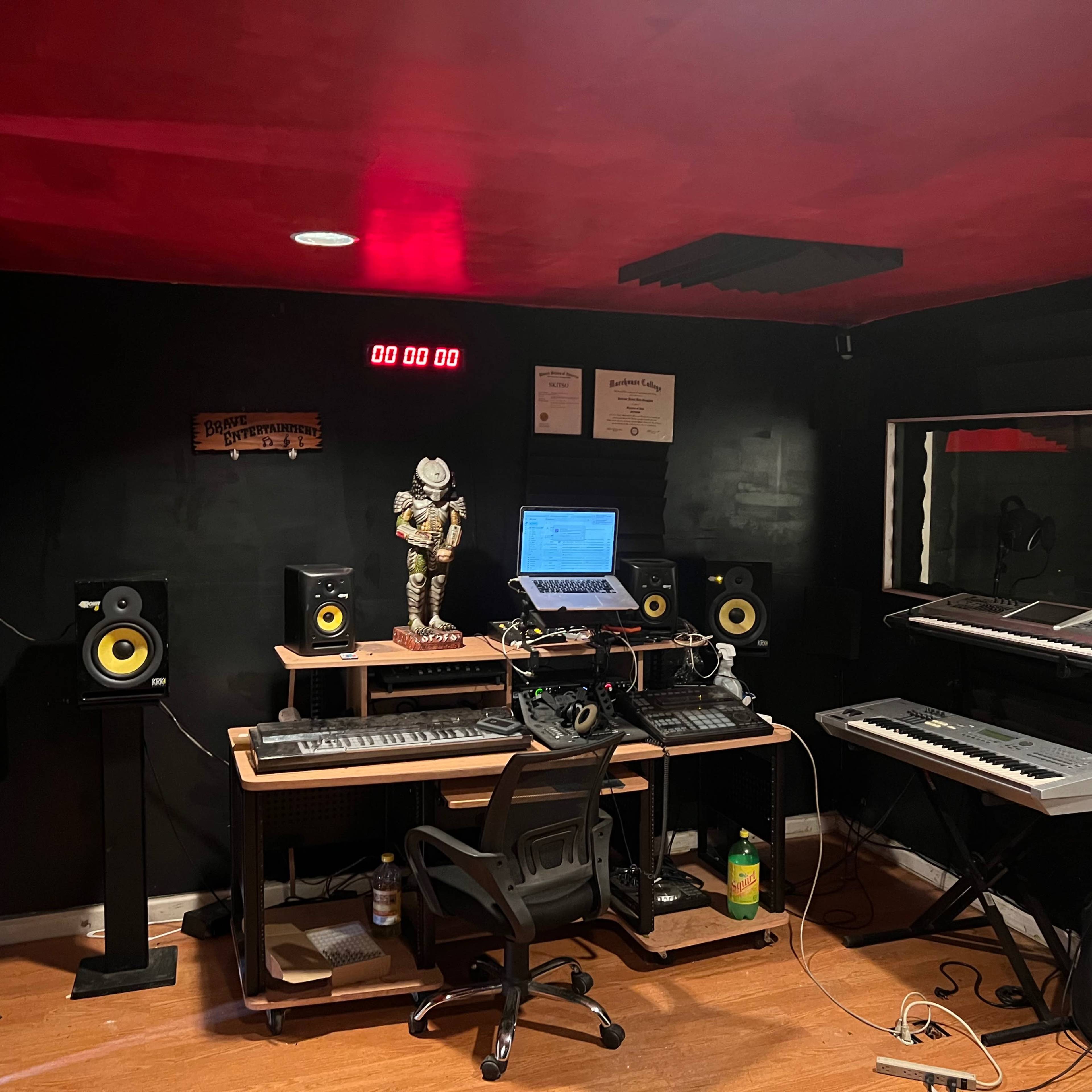 A music production studio equipped with speakers, keyboards, a computer, and a skeleton figurine on the desk.