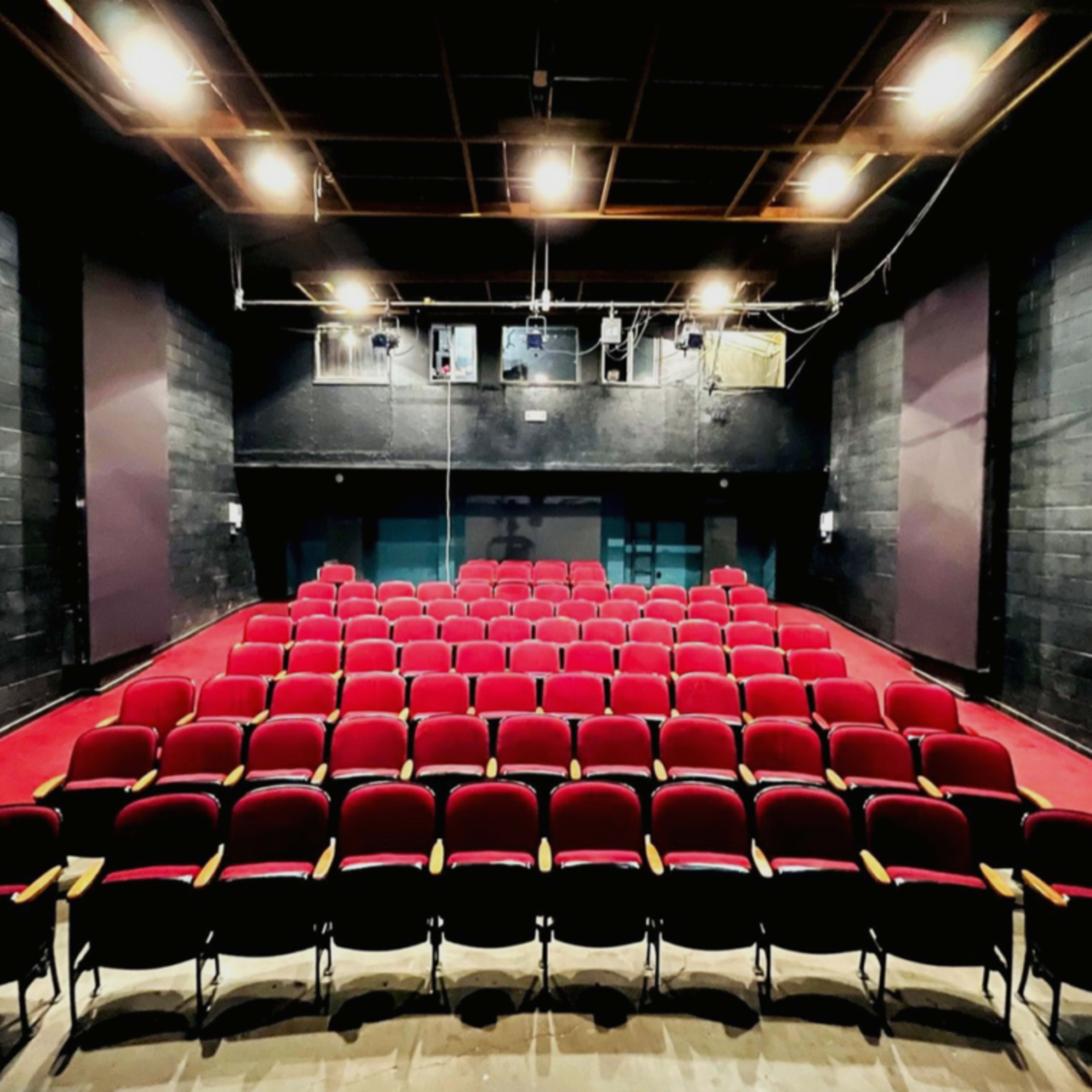 A theater with rows of red seats arranged in front of a dark stage and black walls.