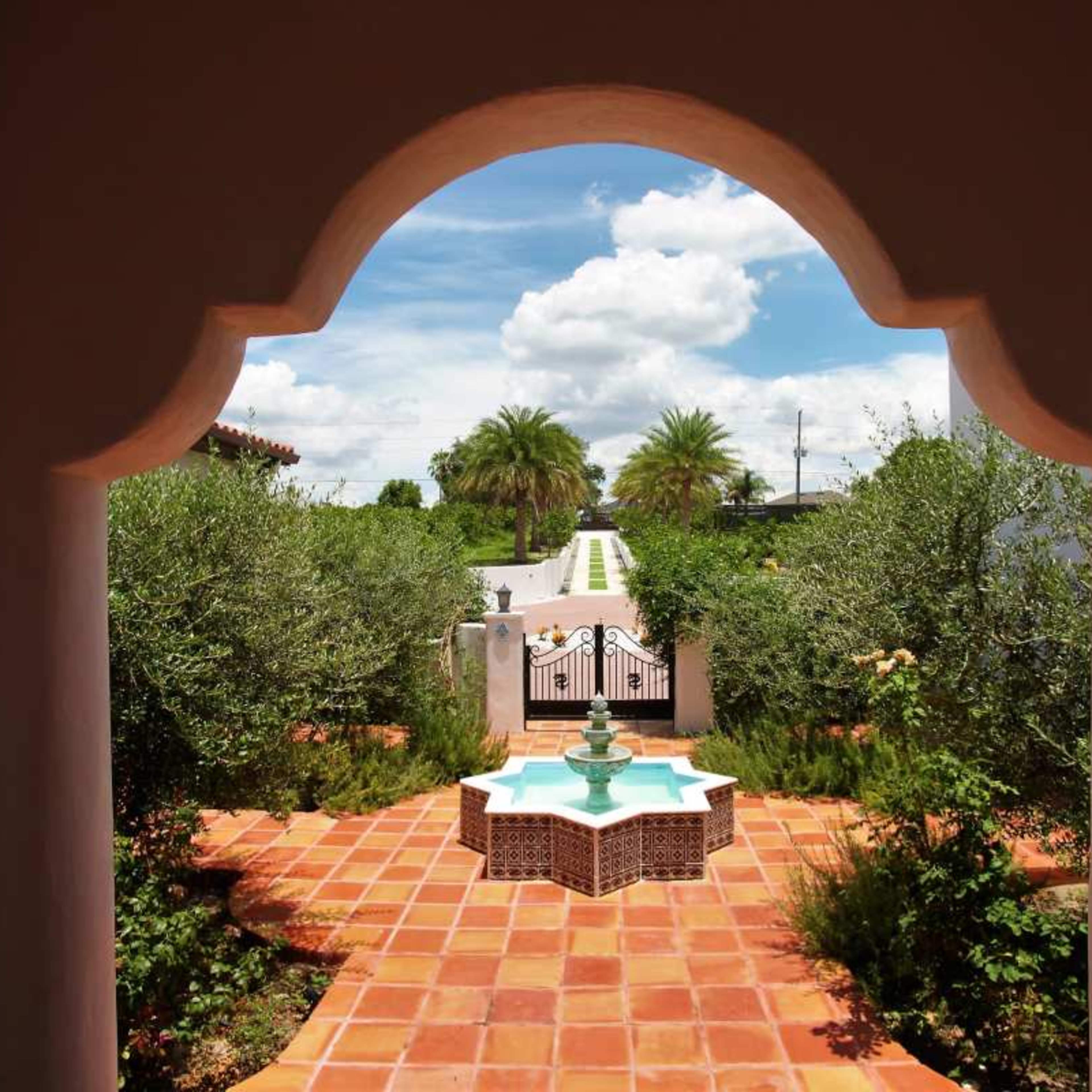 A view of a garden pathway leading to a fountain, framed by an archway.
