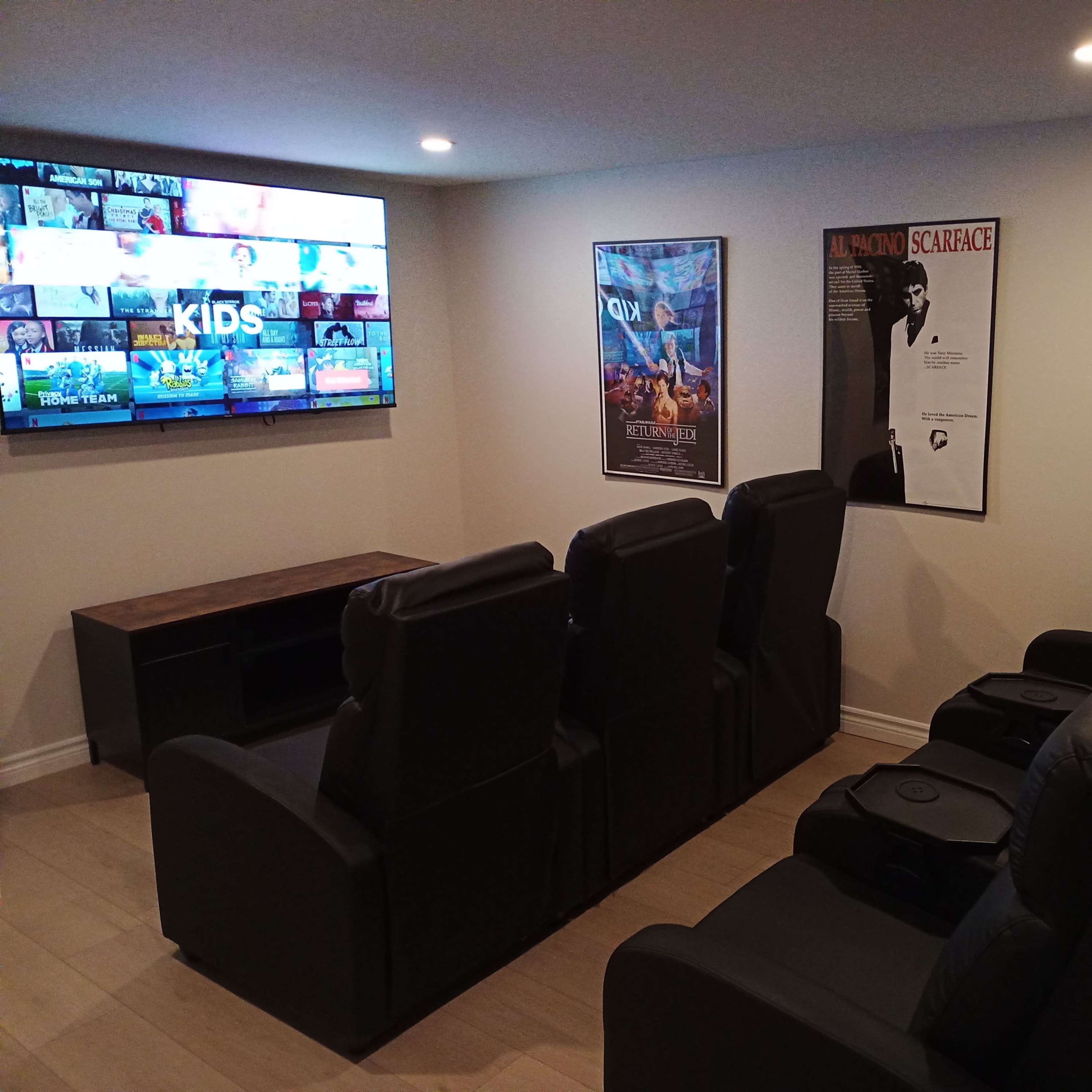 A home theater with black reclining chairs facing a large screen, flanked by movie posters on the walls.